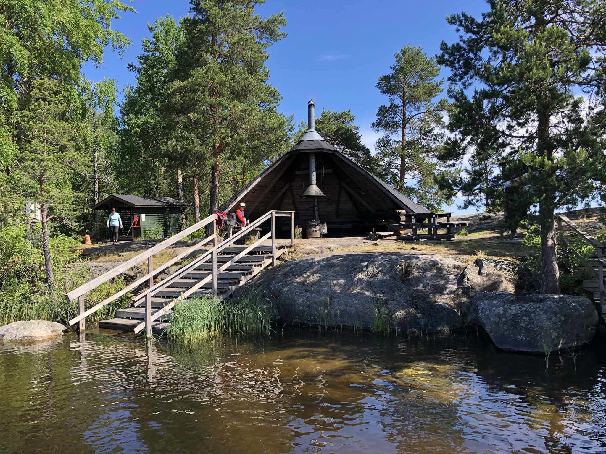 Vesiltä näkymä kalliorannalle, jossa suuri laavukatos, edessä puuportaat.