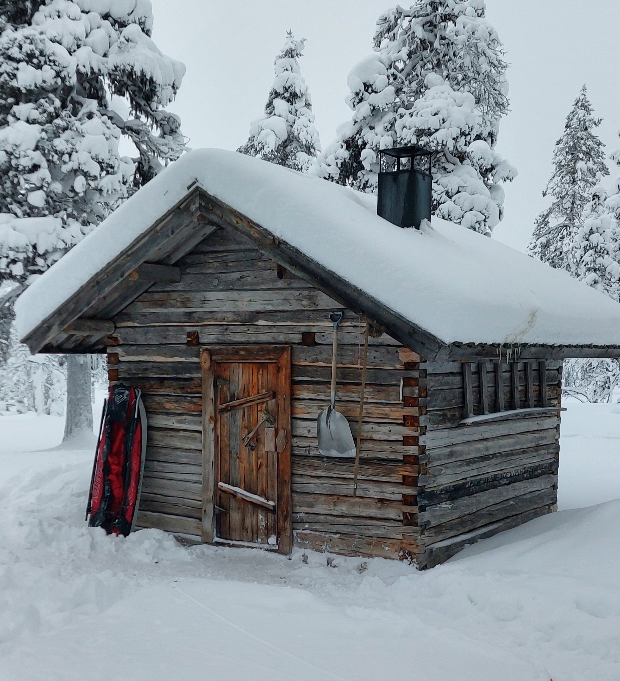 The old log cabin is located in the middle of the snowy forest.