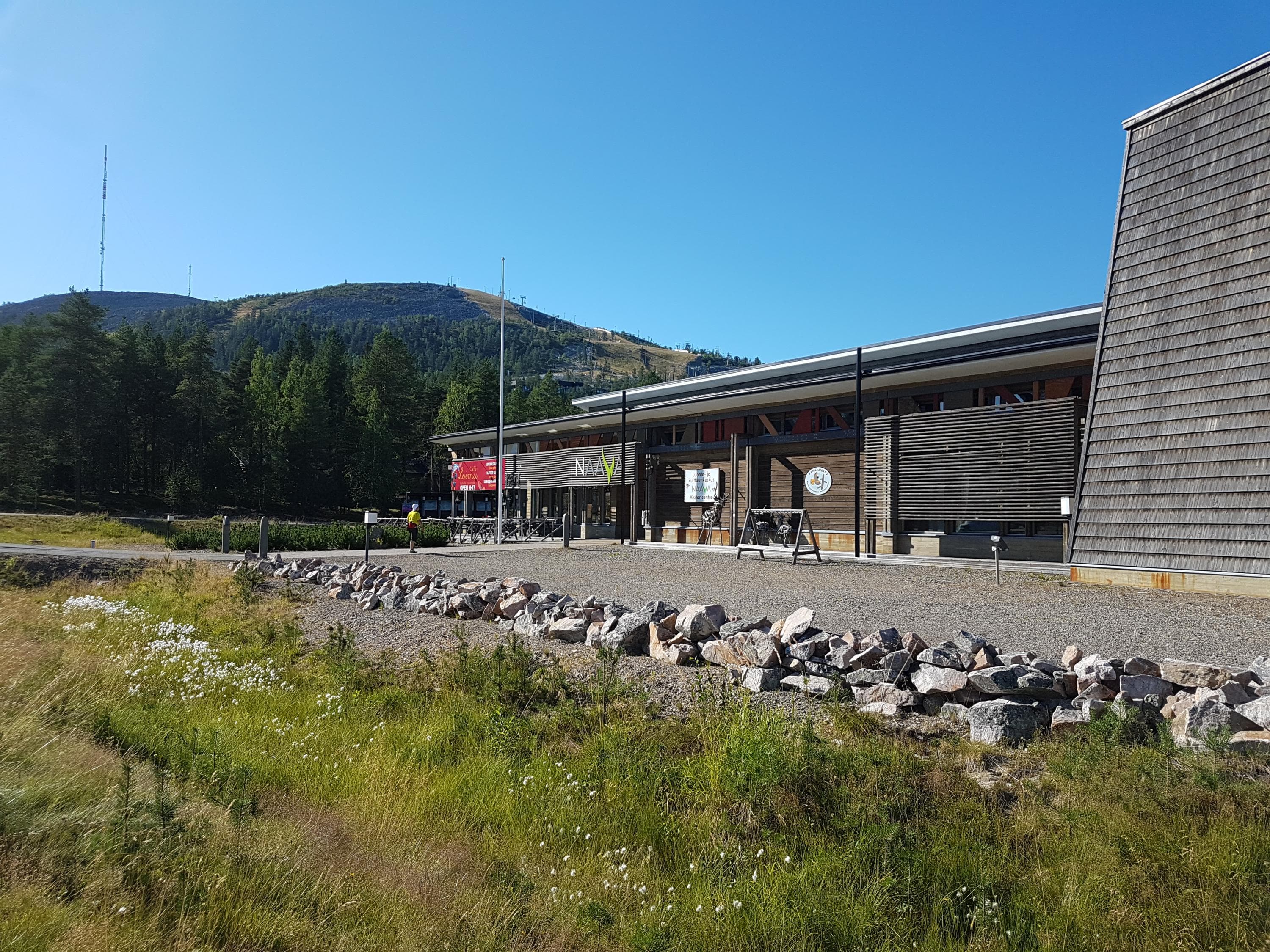 En stor byggnad med träfasad en solig sommardag. Ett fjäll reser sig i bakgrunden.