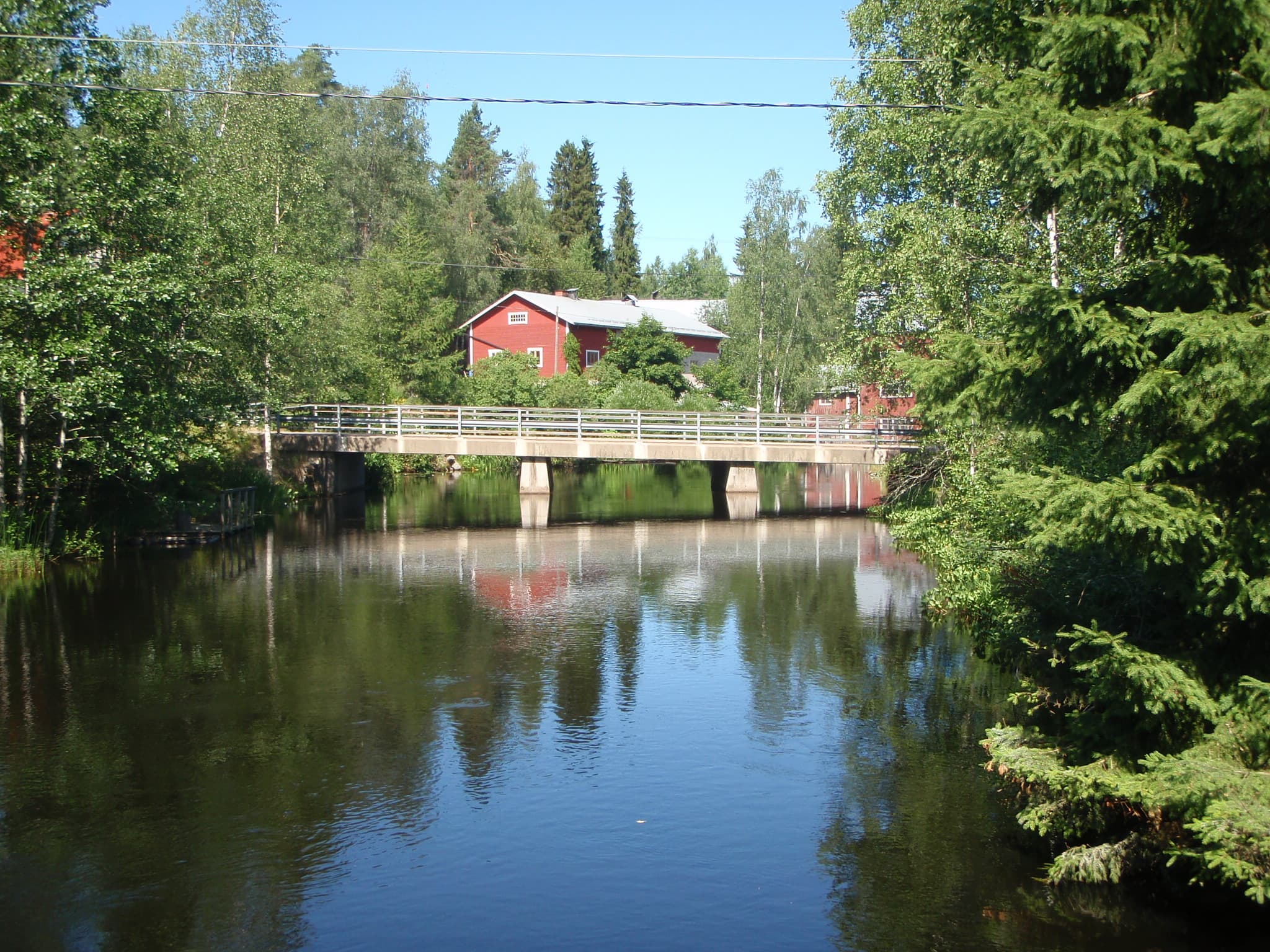 Maantiesilta kapean vesistön ylitse, taustalla punaisia rakennuksia.