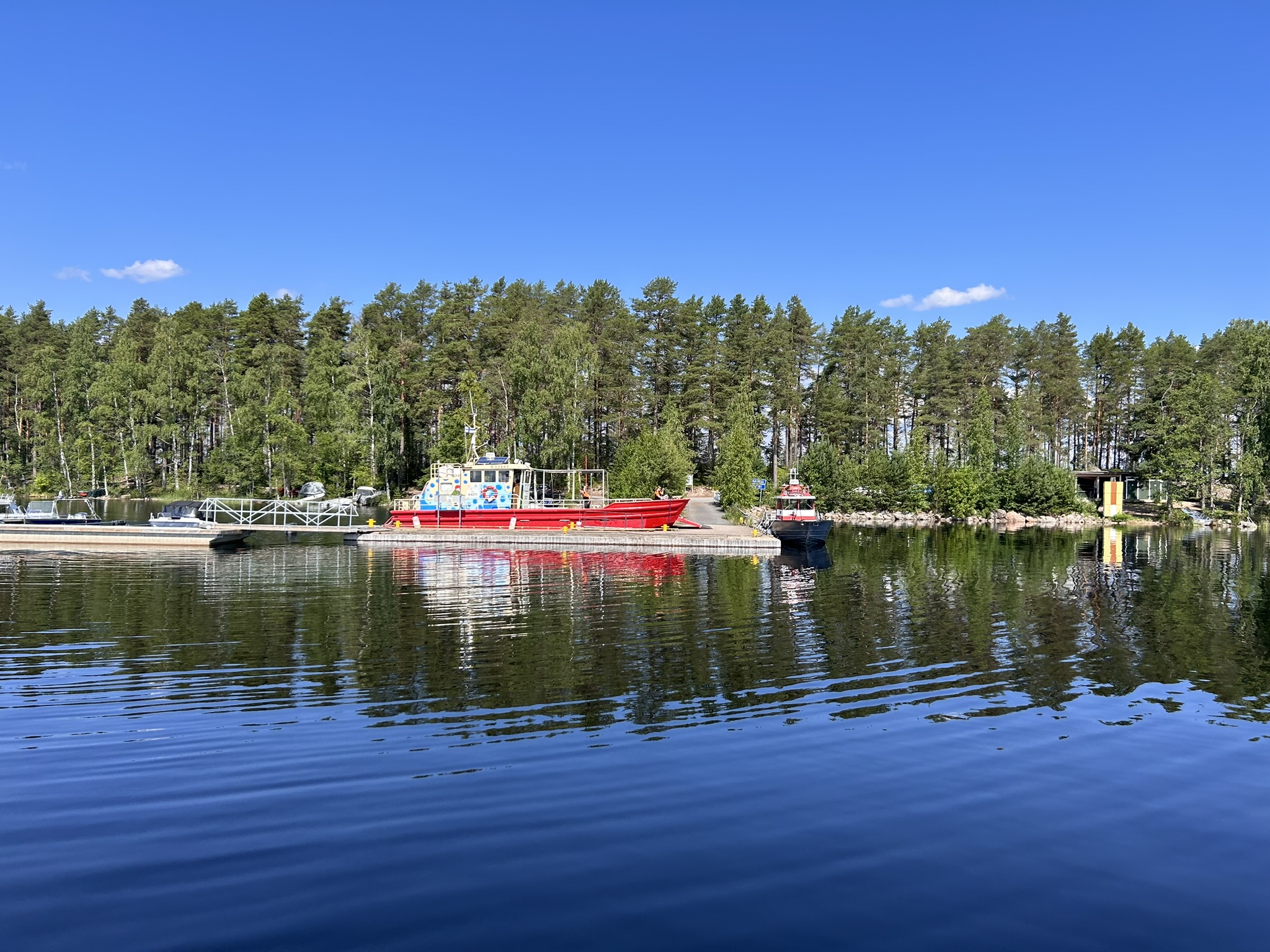 Venesatama vesiltä, laiturissa suuri punainen pyörälautta Rasti. Taustalla mäntypuustoa.