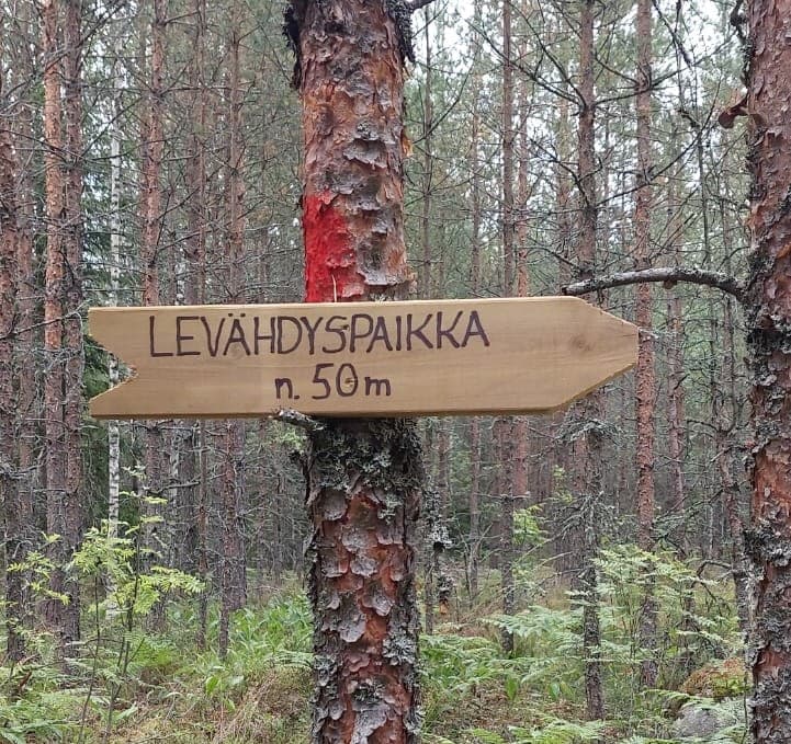 Nuoreen mäntyyn kiinnitetty puinen suuntaviitta, jossa lukee LEVÄHDYSPAIKKA n. 50 m.