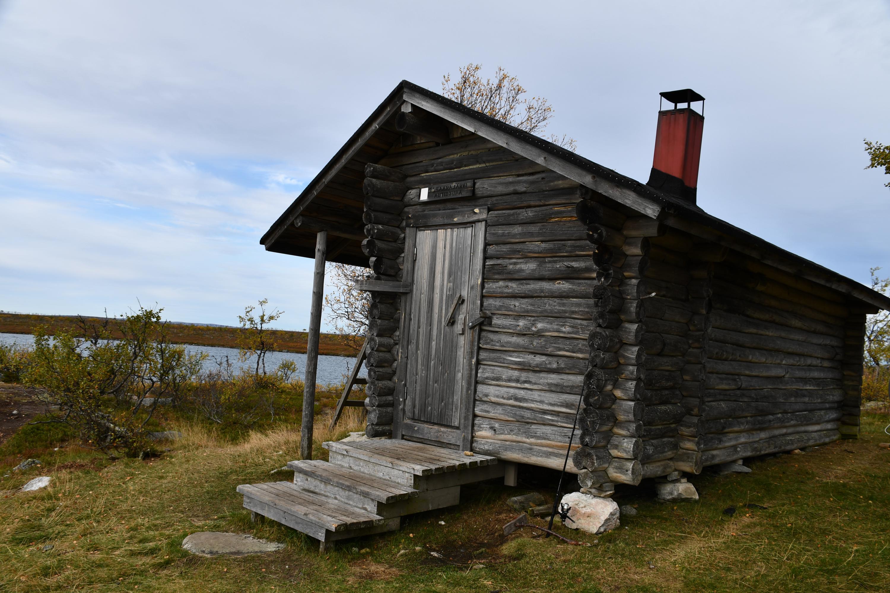 The weathered log cabin is located by the lake.