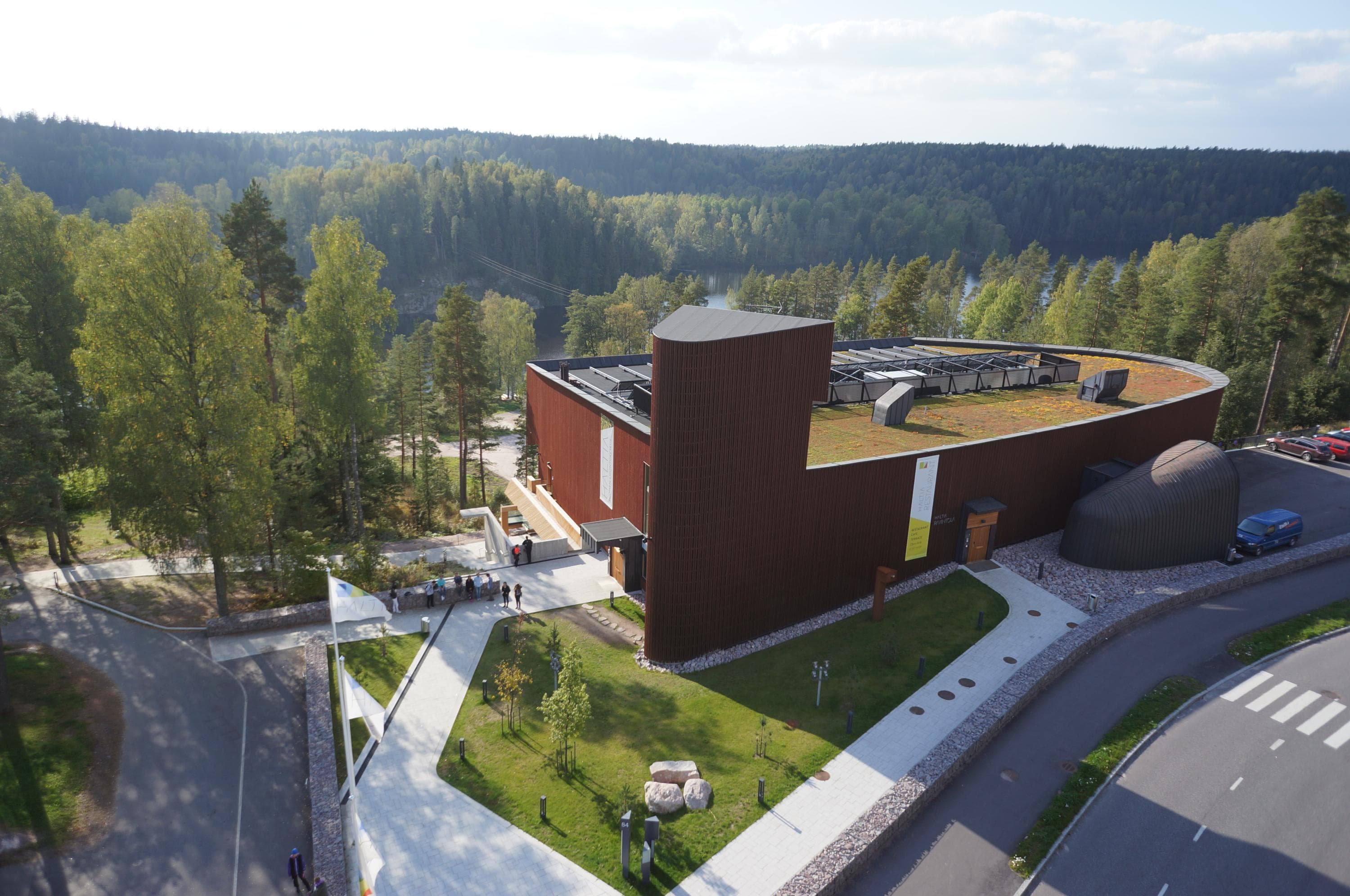 Ilmakuva. Ruskea rakennus jossa on torni toisessa päässä, taustalla vihreä metsä