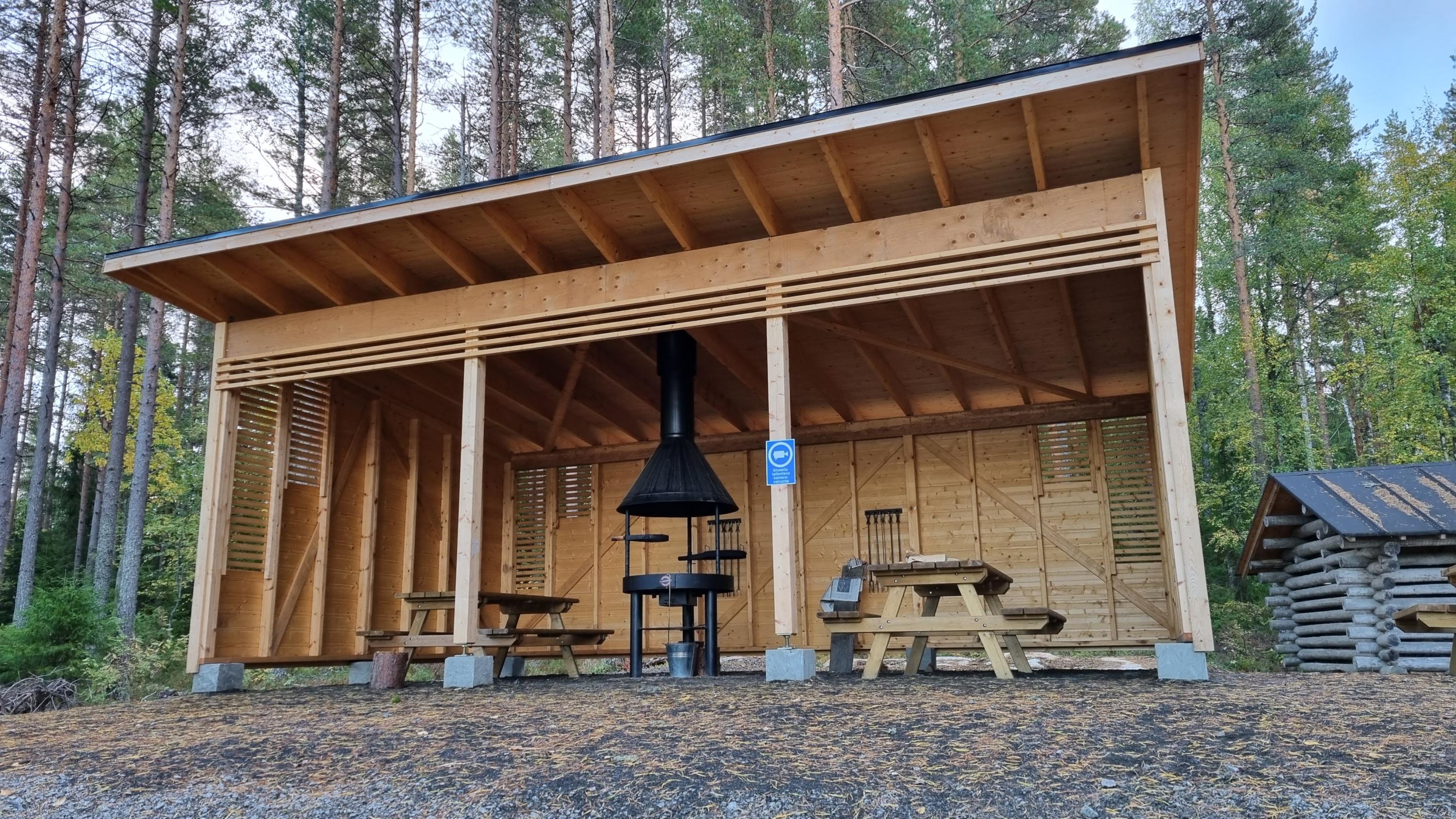 A wooden, open cooking shelter in the forest.