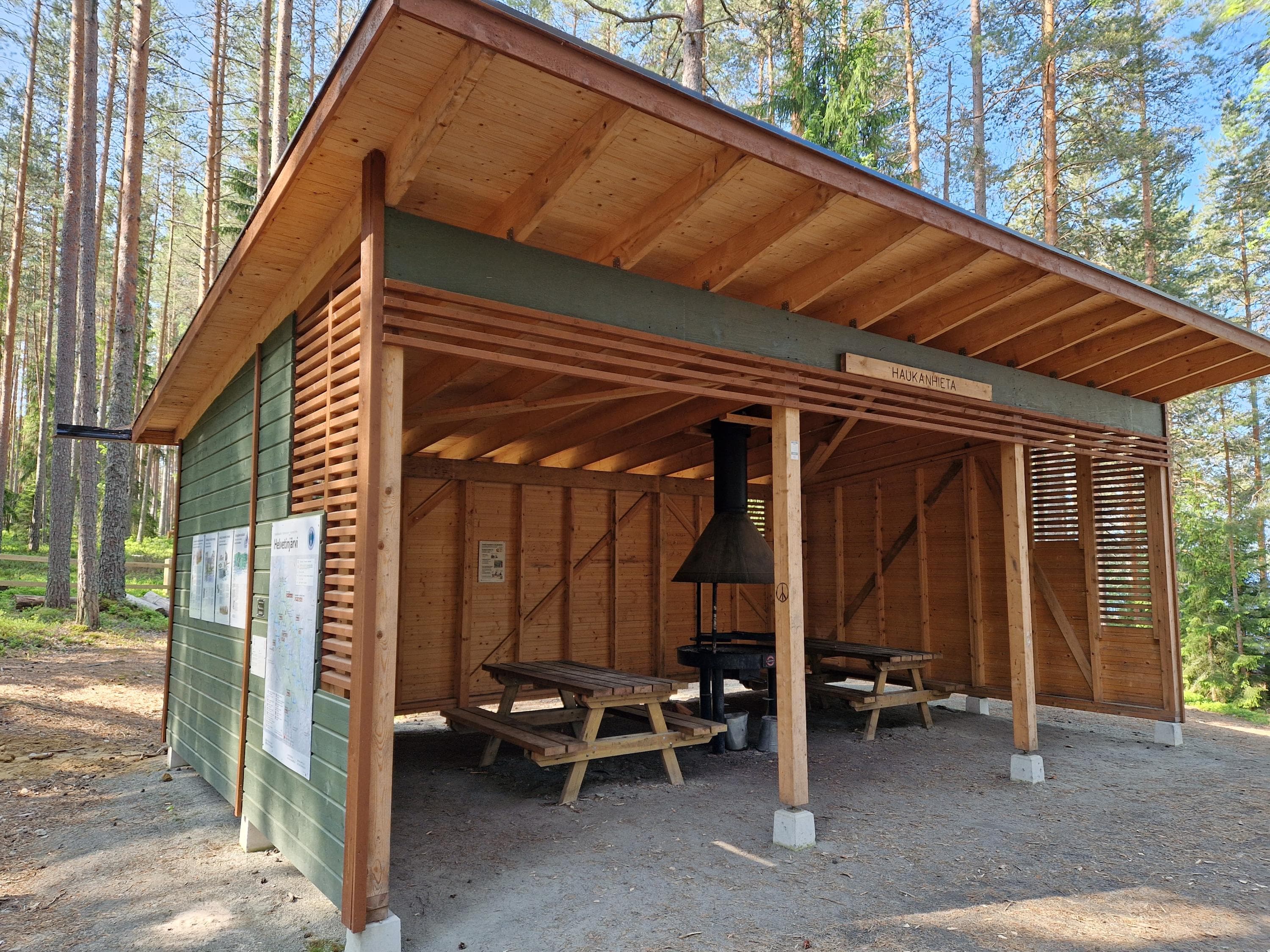  A wooden, open cooking shelter with flat terrain in front.
