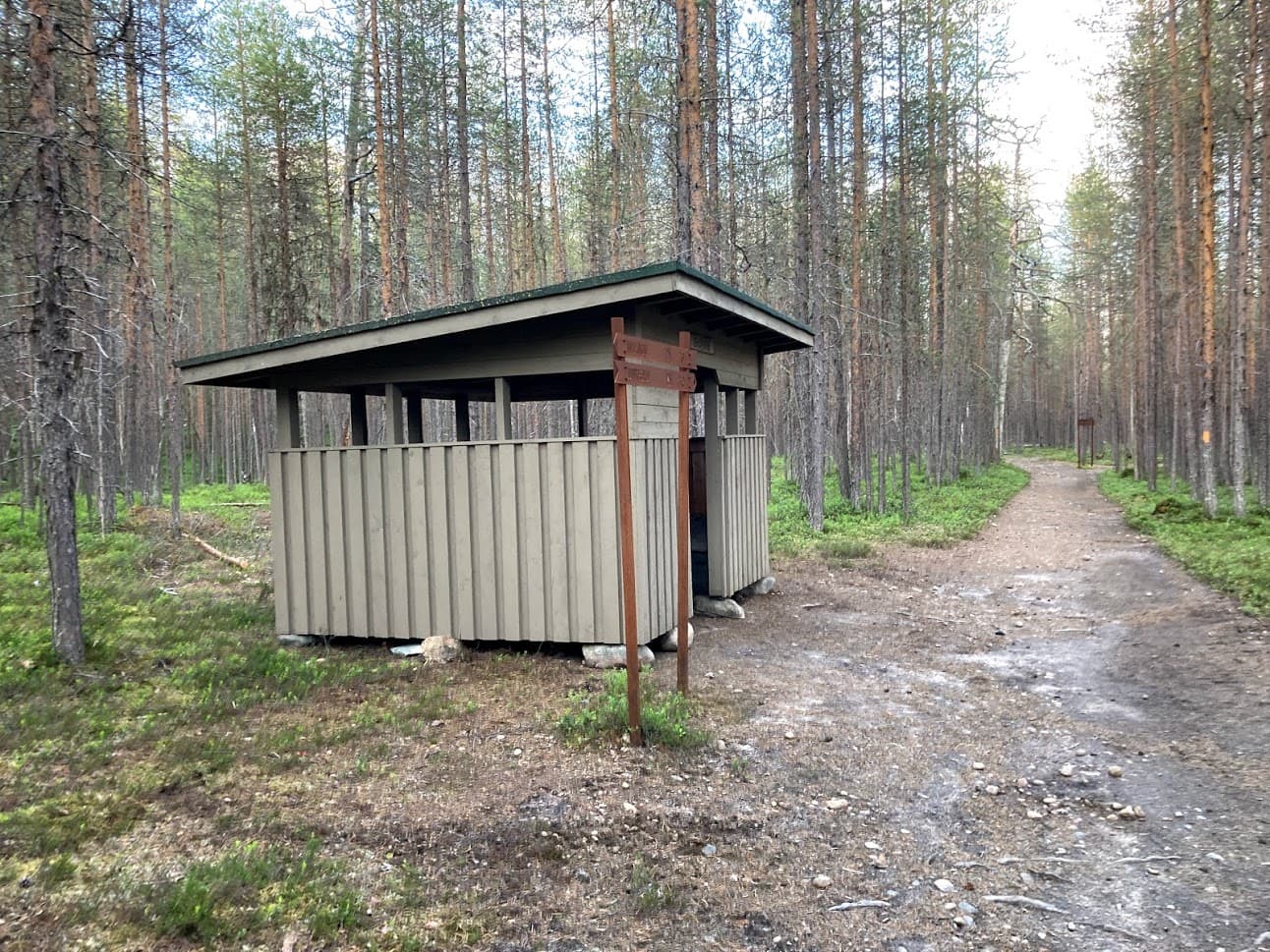 Next to the gravel path, there is a wooden waste shelter.