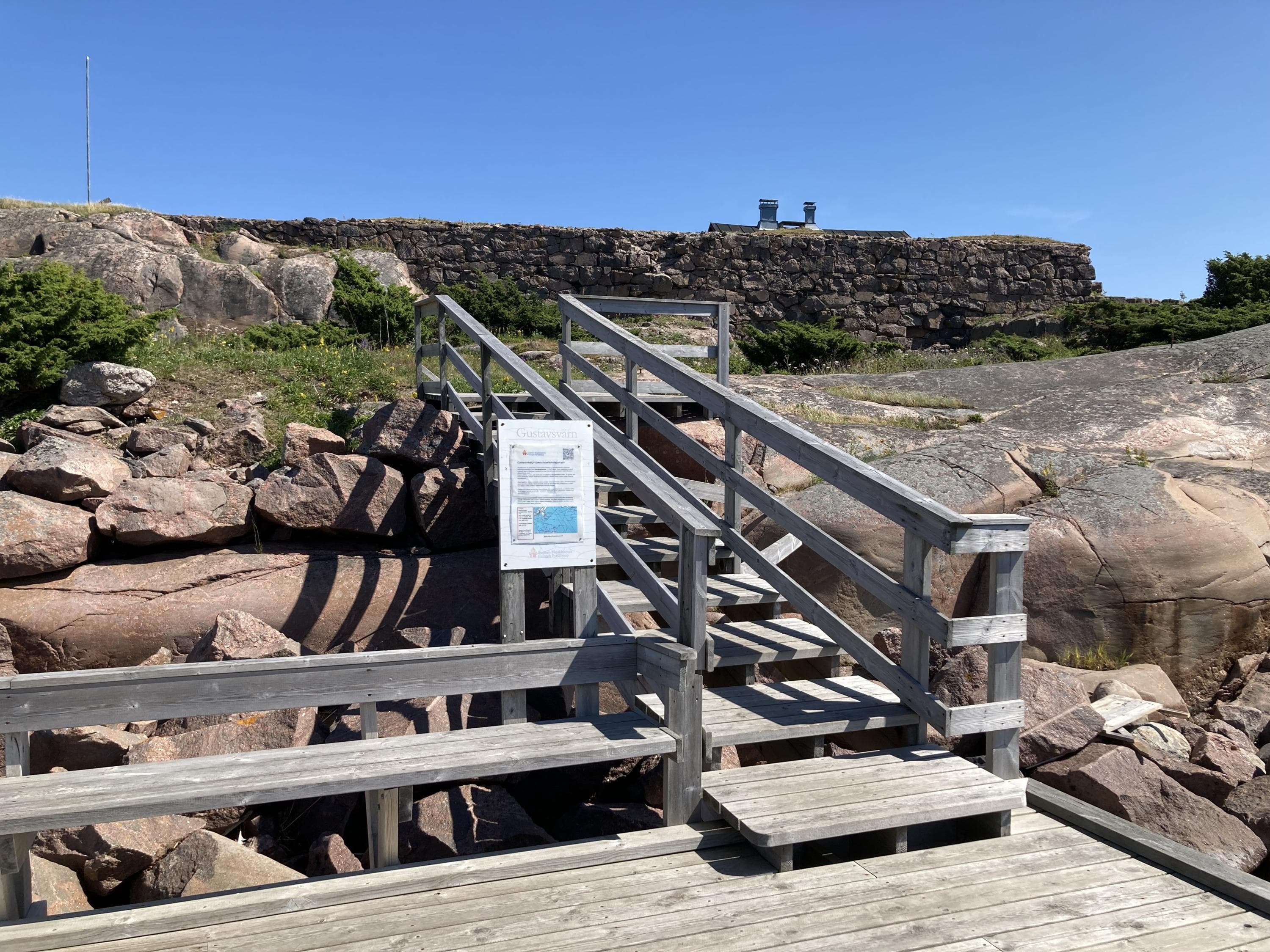 Från bryggan vid klippstranden leder en trätrappa upp mot fästningsruinen på ön.