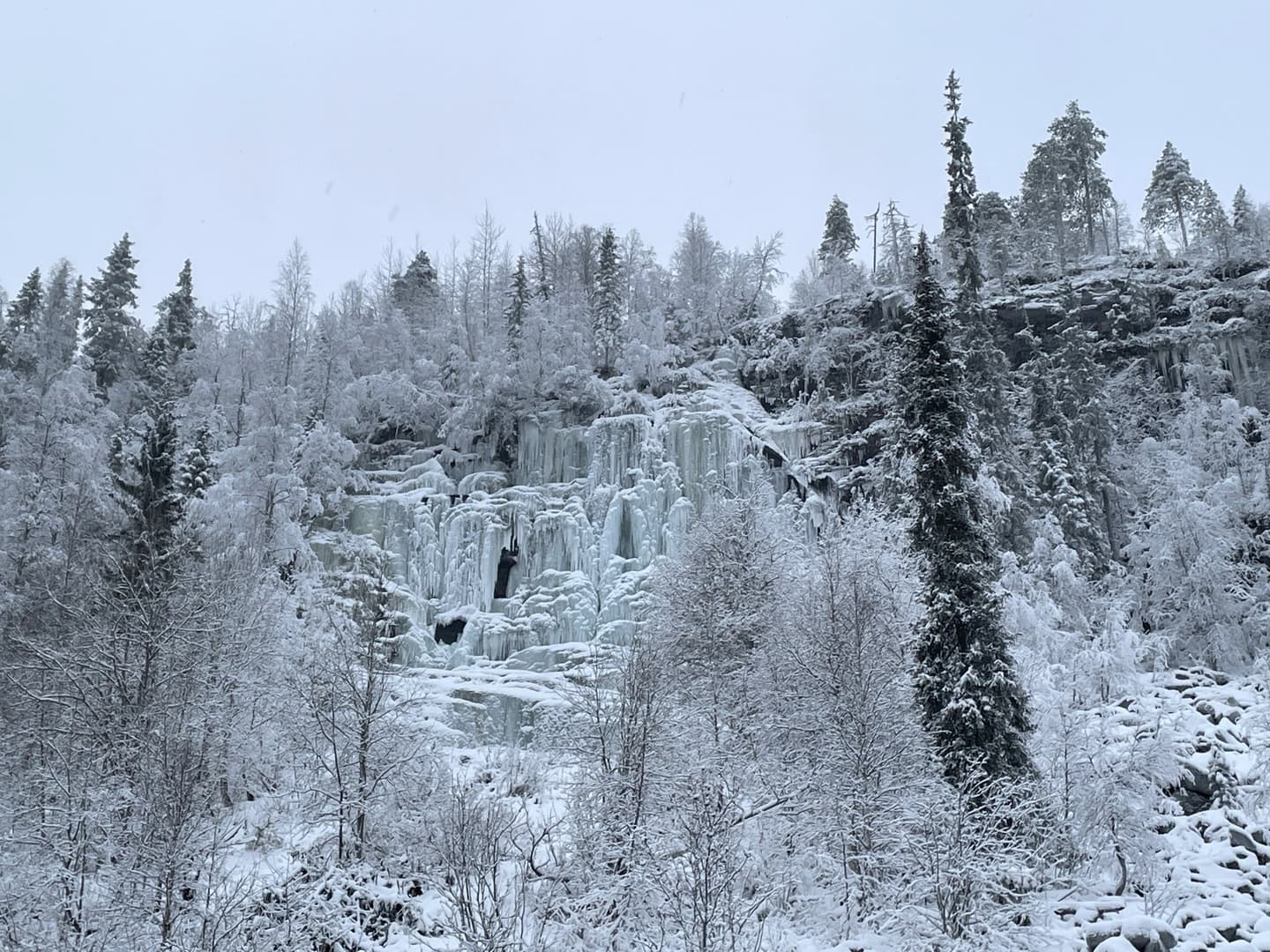 A bluish icefall in early winter. There is little snow on the trees.