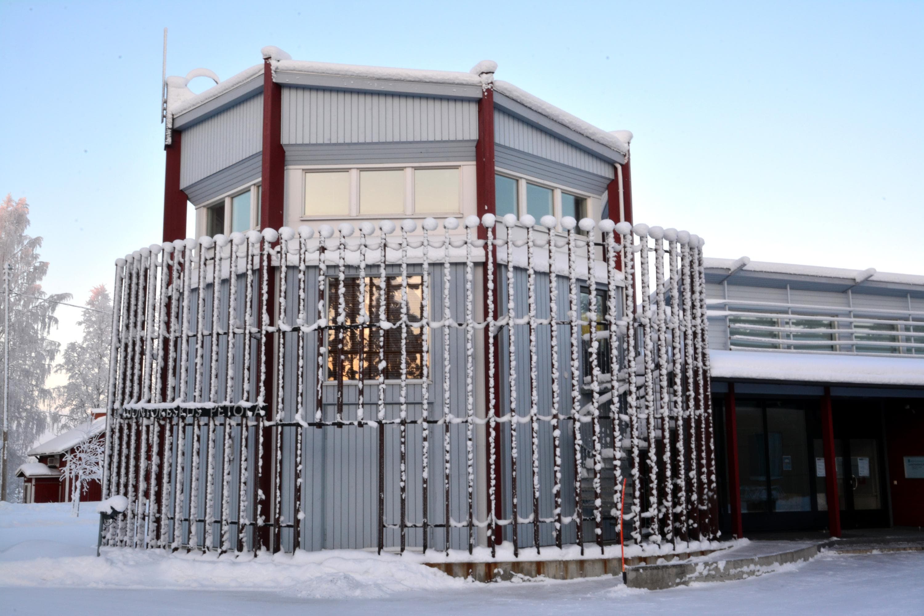 Keskellä rakennus, alaosassa luminen maa. Taustalla taivas.