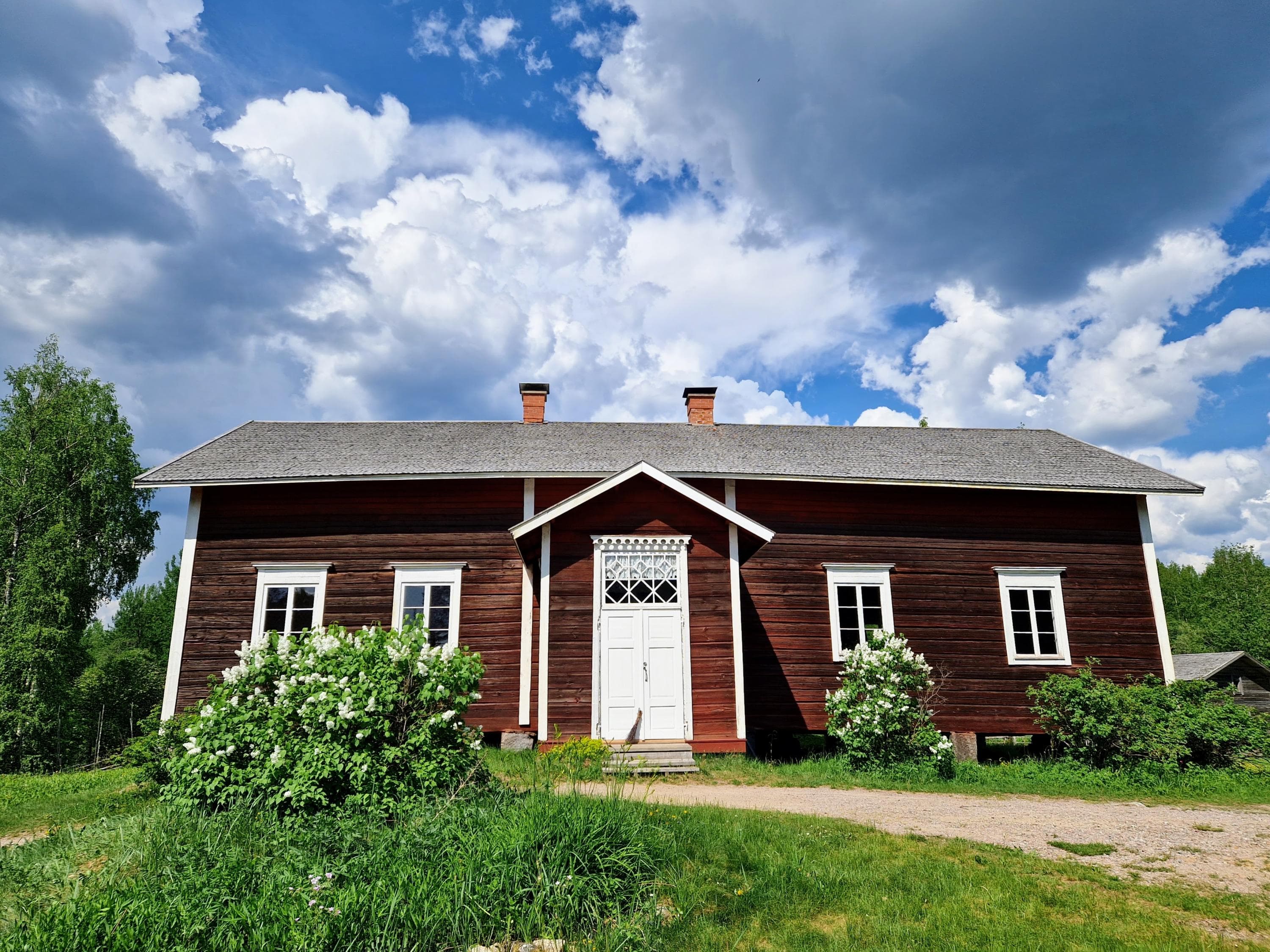 Punainen hirsirakennus ja vehreä pihapiiri kesäaikaan.