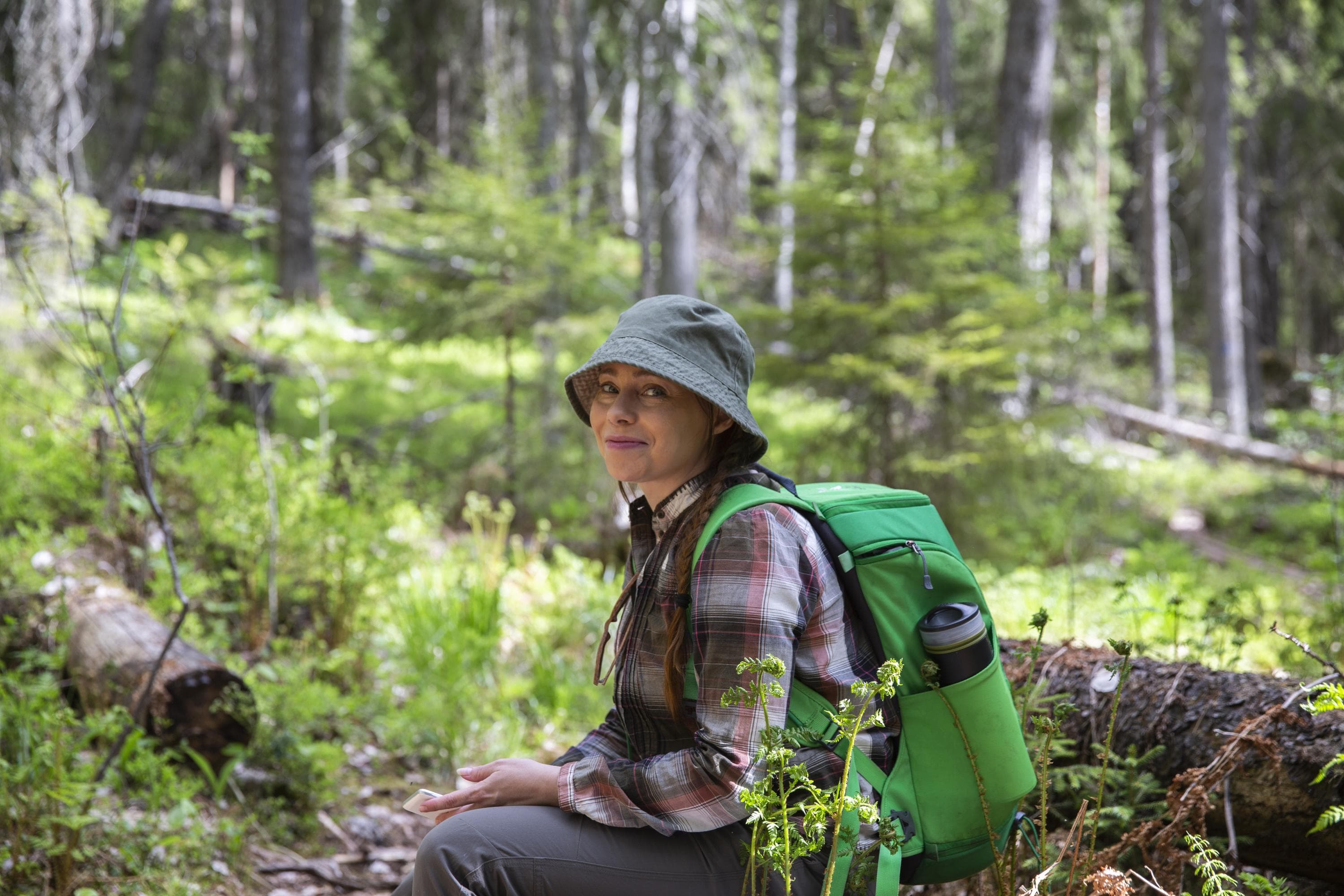 Reppuselkäinen retkeilijä istuu keväisessä metsässä.