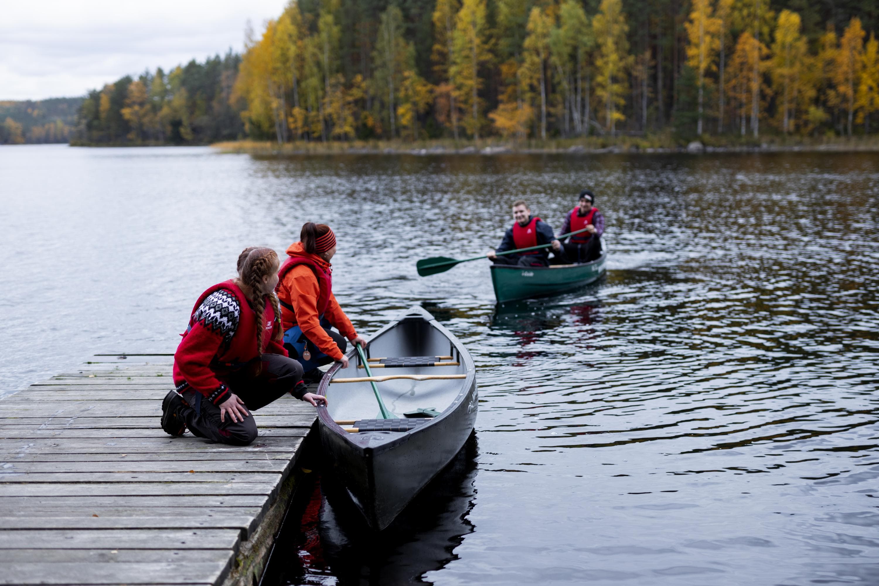 Kaksi retkeilijää meloo laituriin. Kaksi retkeilijää ja kanootti ovat jo laiturissa.