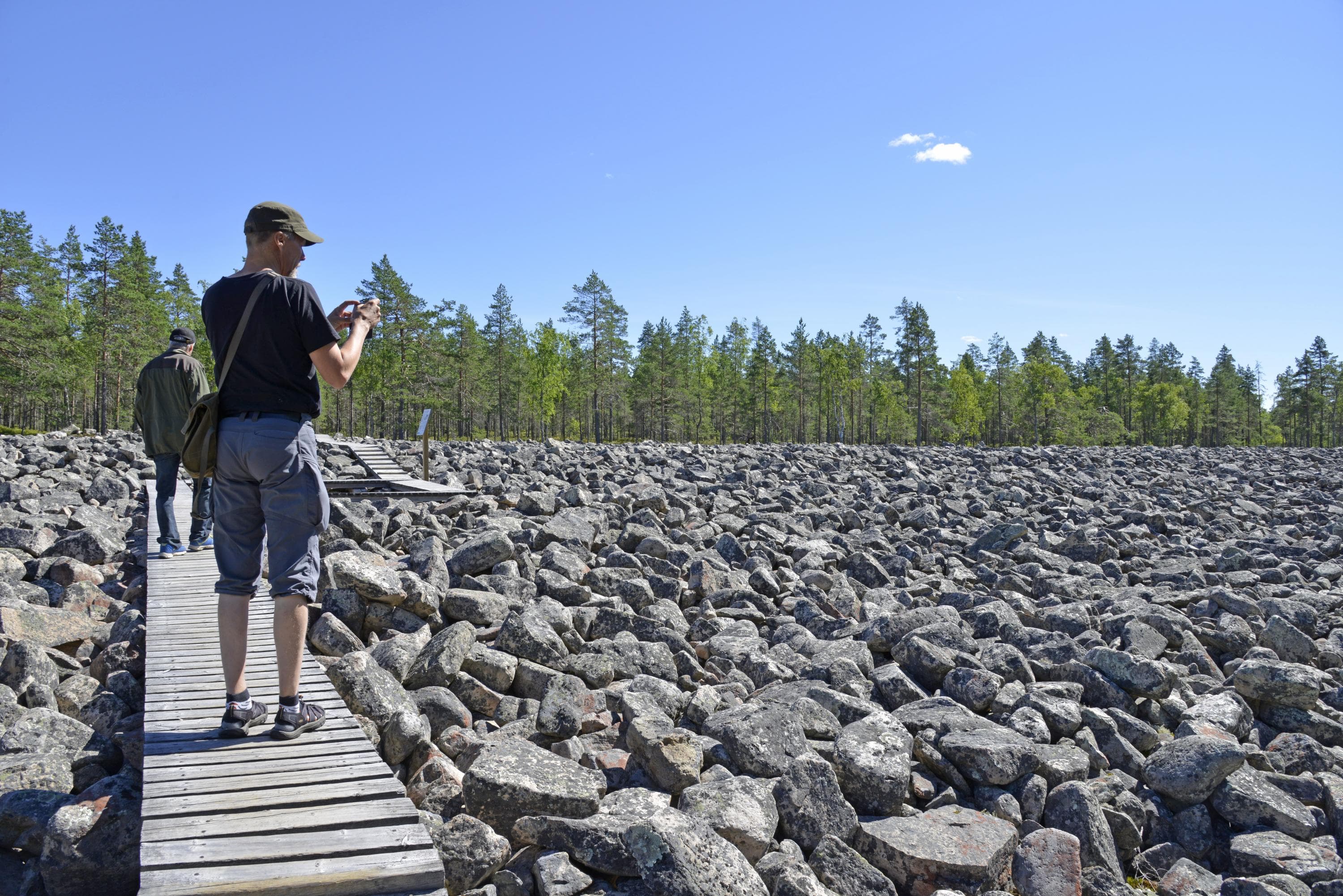 Two men on duckboards. The man in the front is taking a picture of the stones.