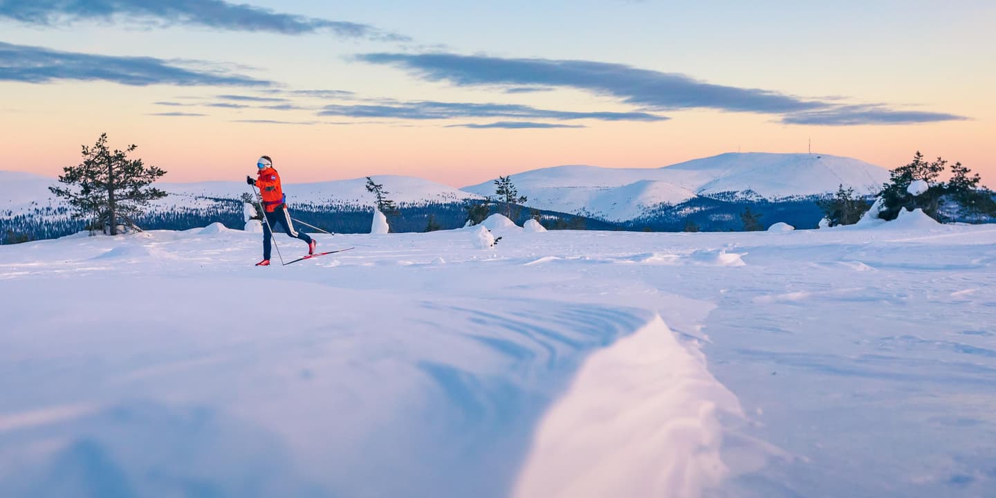 Image: Rami Valonen / Metsähallitus A skier is skiing on the top of a fell. More fells can be seen on the horizon. The sky is colorful.