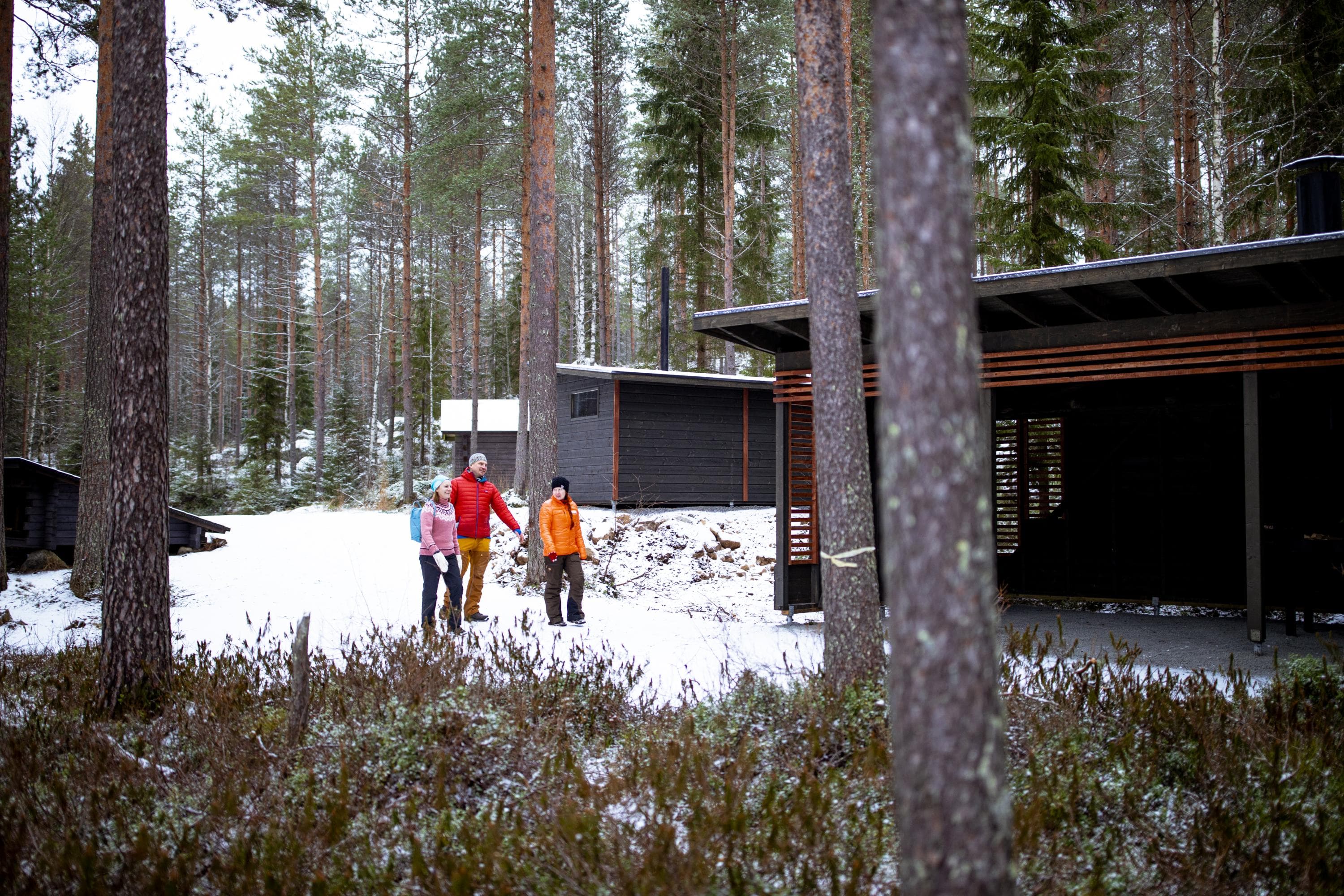 Kuva: Maarit Vaahteranoksa Kolme retkeilijää kävelee taukopaikan rakennusten edessä. Maassa on vähän lunta.