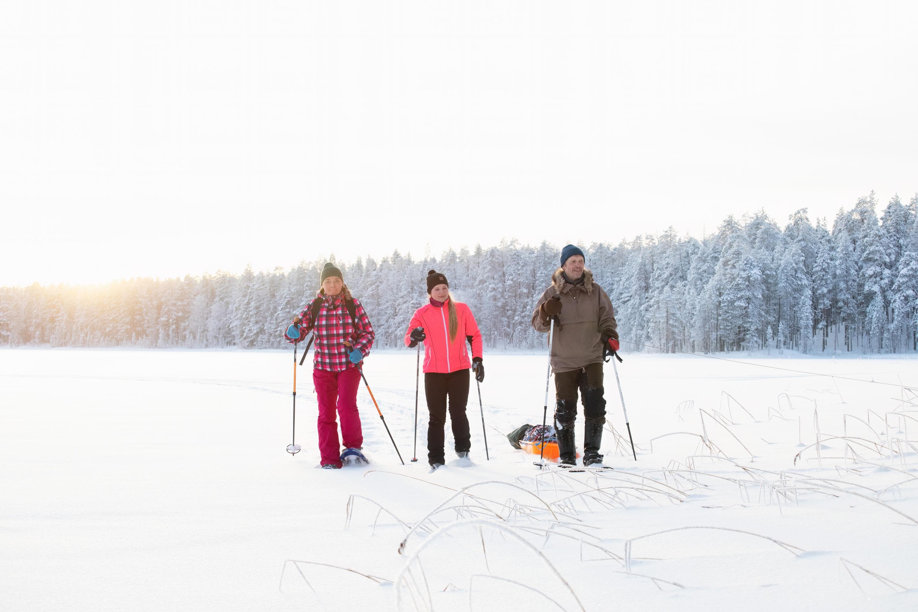 Image: Kuvatoimisto Keksi Three hikers walk on snowshoes on a snowy lake. One of them has a sled.