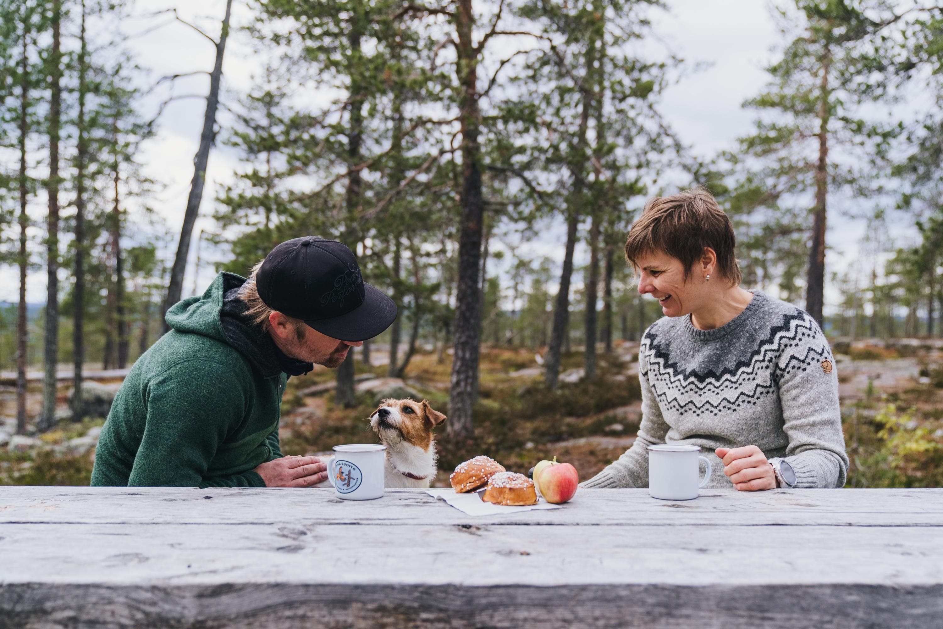 Kuva: Jaakko Posti Kaksi retkeilijää ja koira evästauolla Napapiirin retkeilyalueella syksyisessä mäntymaisemassa.