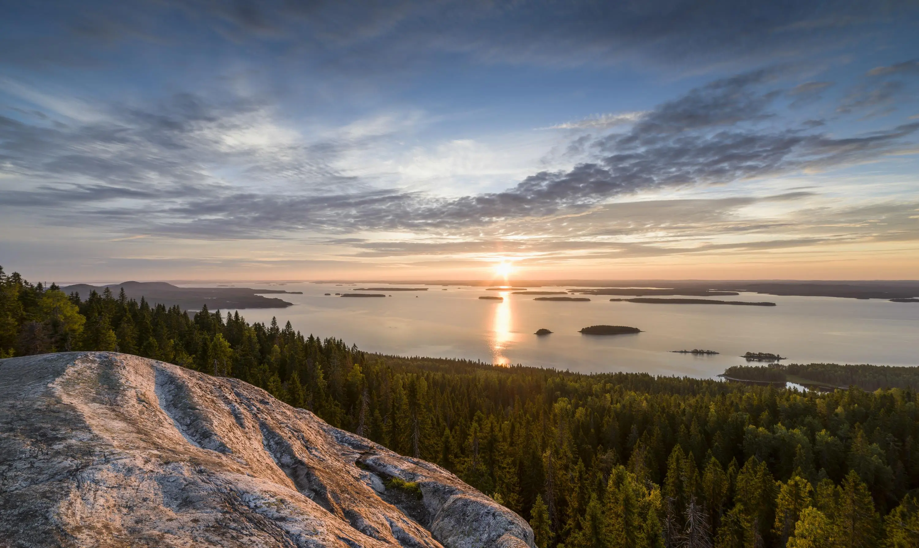 In the foreground, there is a rock and forest, with a lake view in the background. The sun is rising.