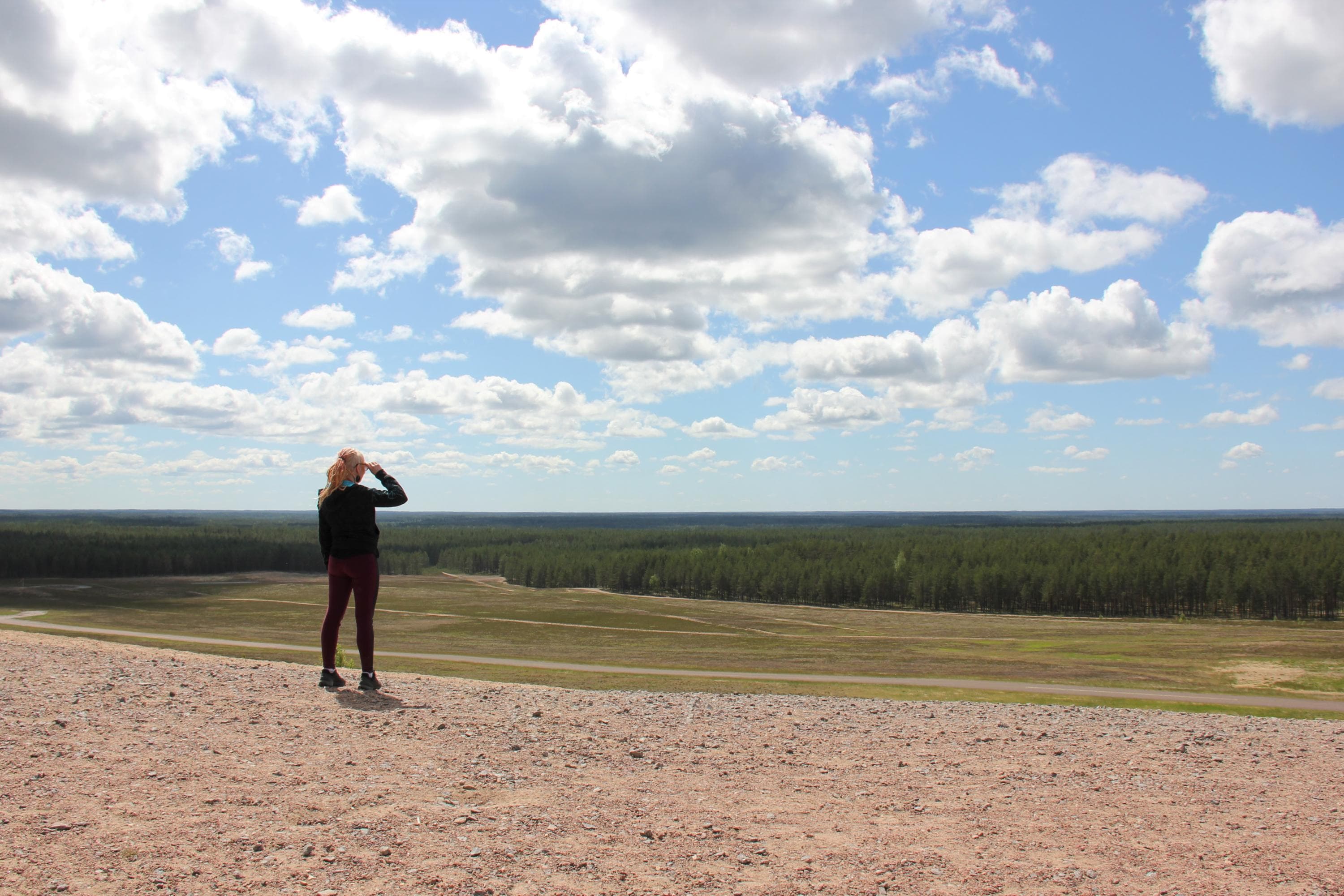 Kuva: Johanna Väkeväinen Retkeilijä katsoo yli avaran nurmikentän kohti metsän rajaa.