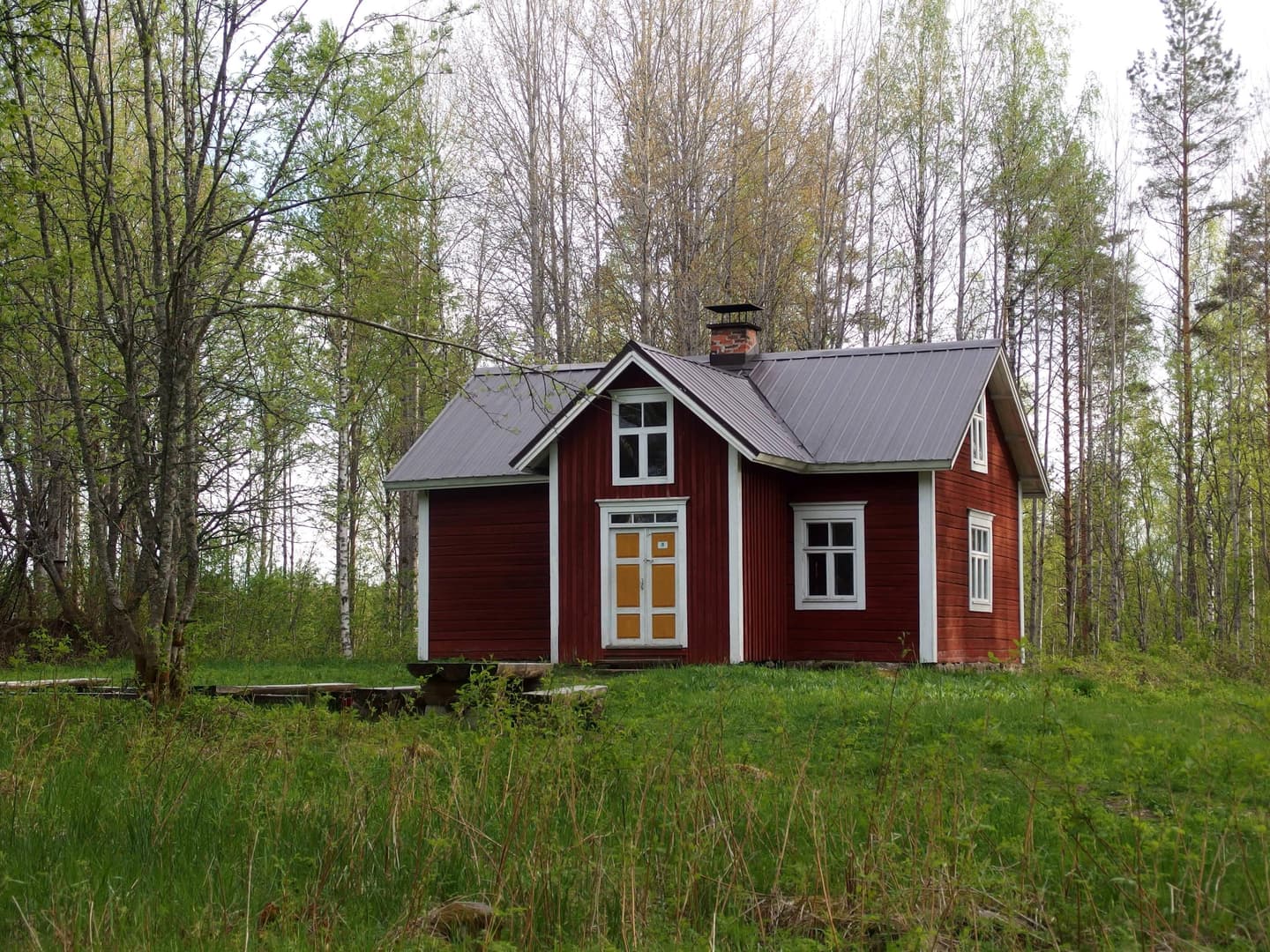 Bild: Sanna-Mari Kunttu Trähus mitt på gräsmattan. Lövträd i bakgrunden.
