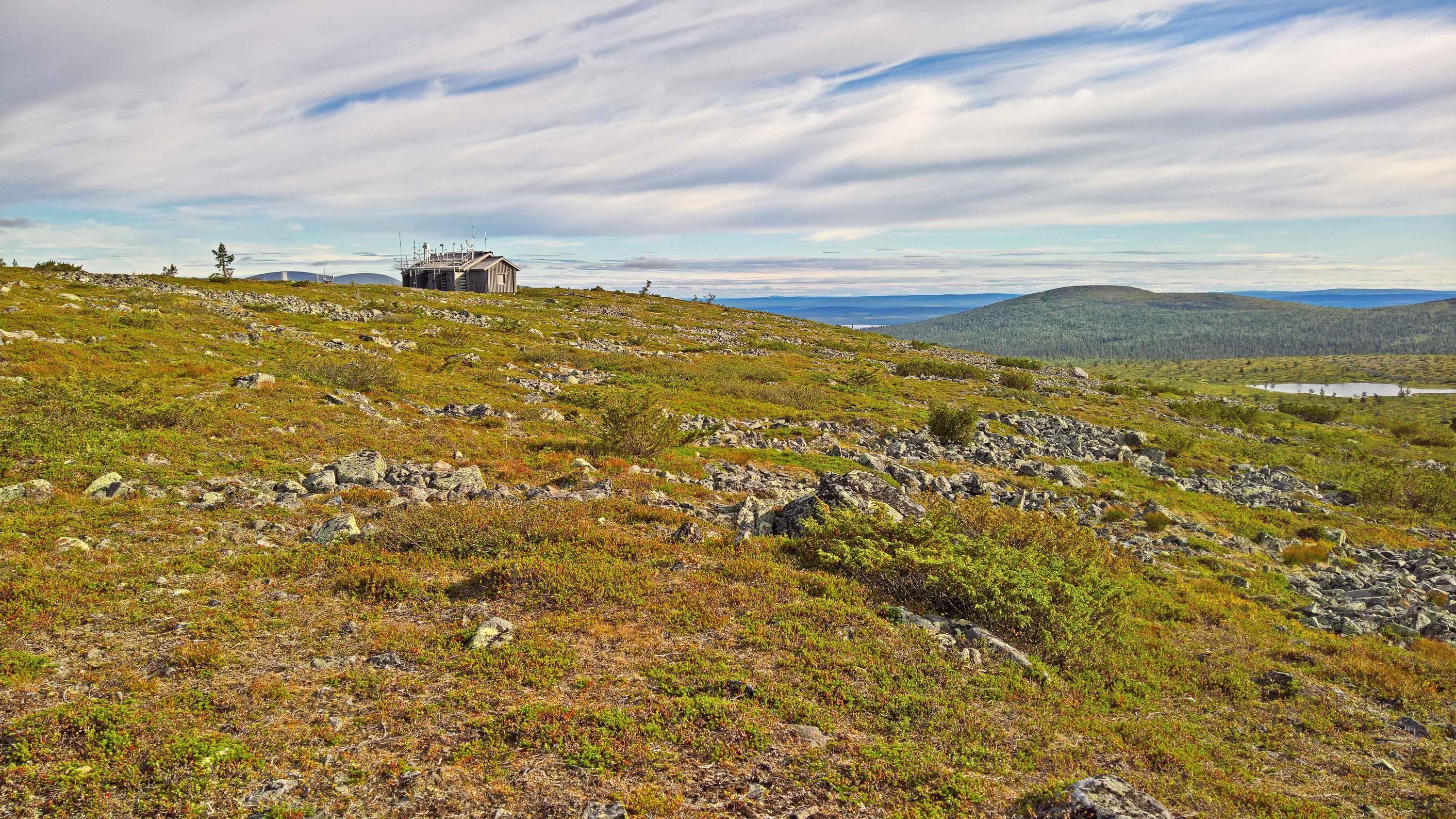 Kuva: Valtteri Hyöky Kuvassa tunturin rinnettä. Kauempana tunturin päällä hirsinen rakennus, jonka katolla tutkimuslaitteistoa.