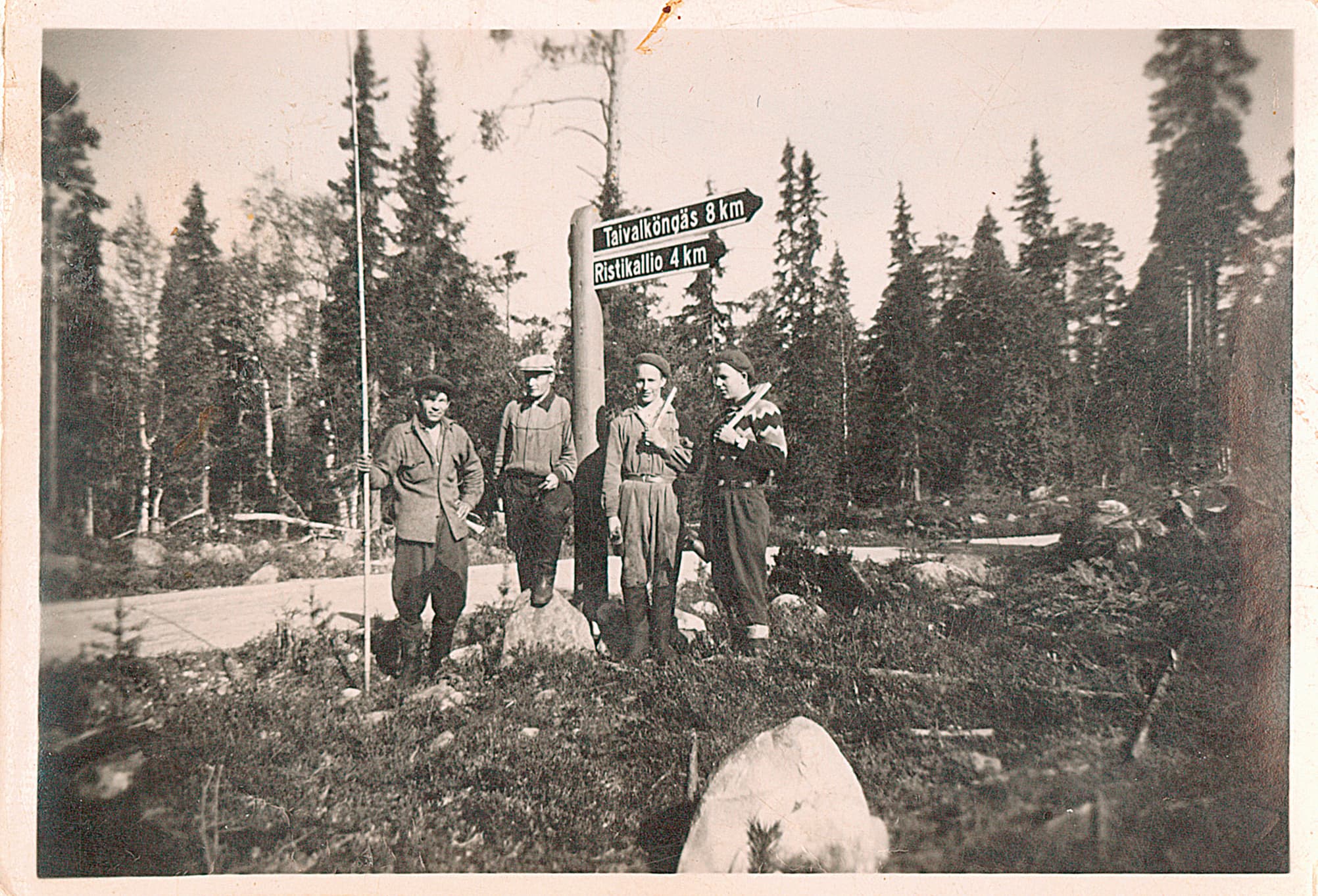 Kuva: Niilo Määttä Vanha mustavalkokuva, jossa neljä työntekijää seisoo rivissä tienviitan edessä ja katsoo kameraan.