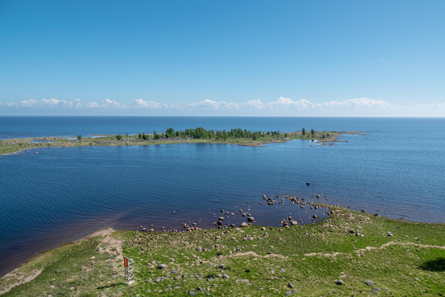 Image: Ismo Lampi The sea is calm and the sky is blue. Land in the foreground and an island next to a narrow area of water.