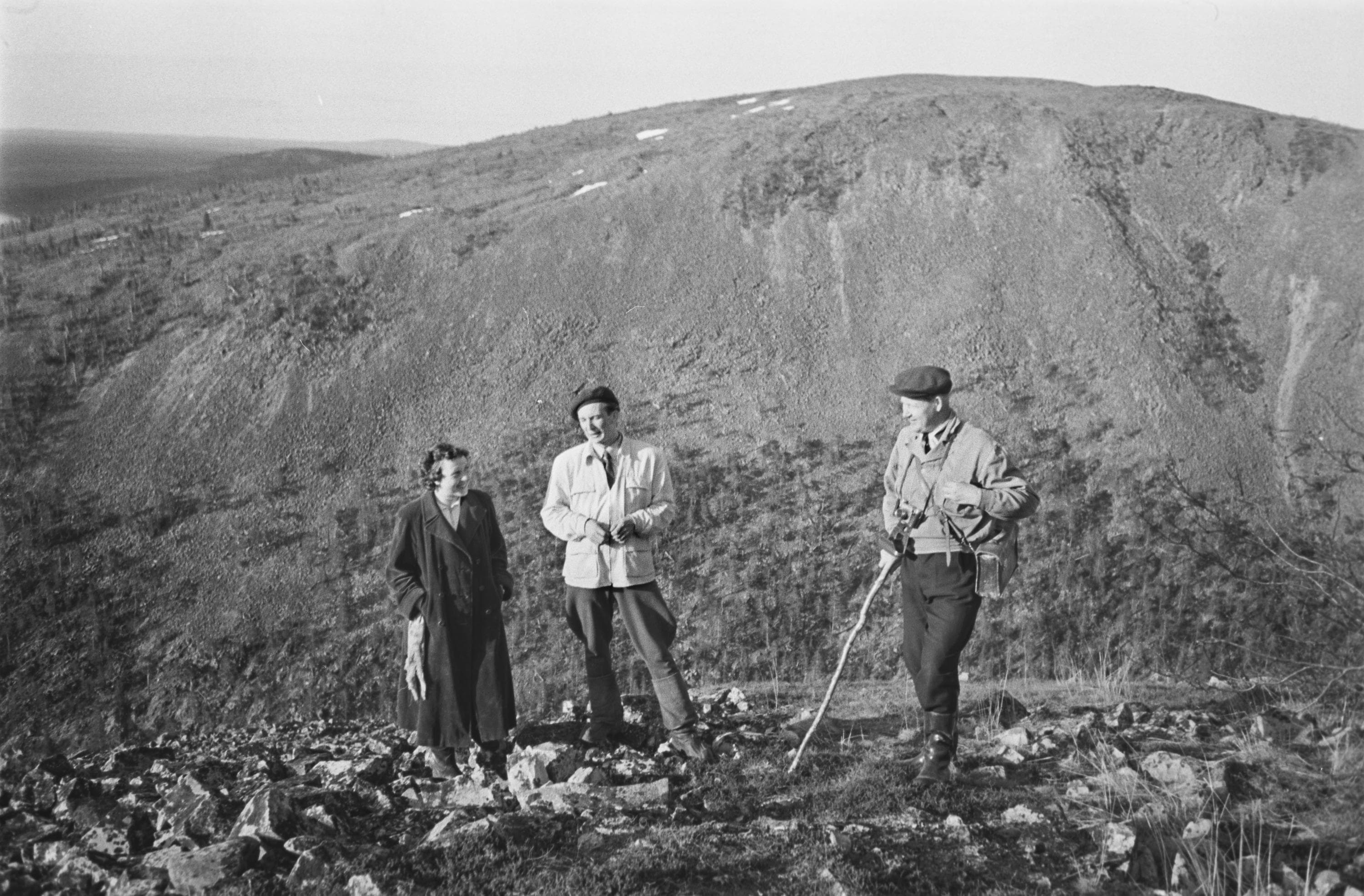 Kuva: Matti Poutvaara, Museovirasto Mustavalkoinen vanha kuva, jossa kolme ihmistä seisoo korkealla kivikkoisessa maastossa, taustalla on tunturi. Sää on poutainen.