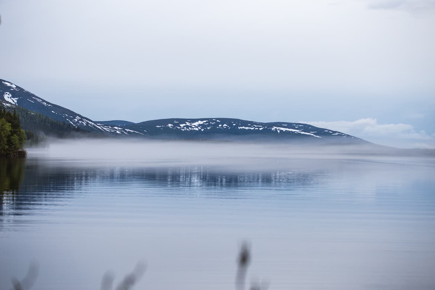 Image: Heikki Sulander The picture shows a lake surface covered in mist. In the background, there are fells with patches of snow on their slopes.
