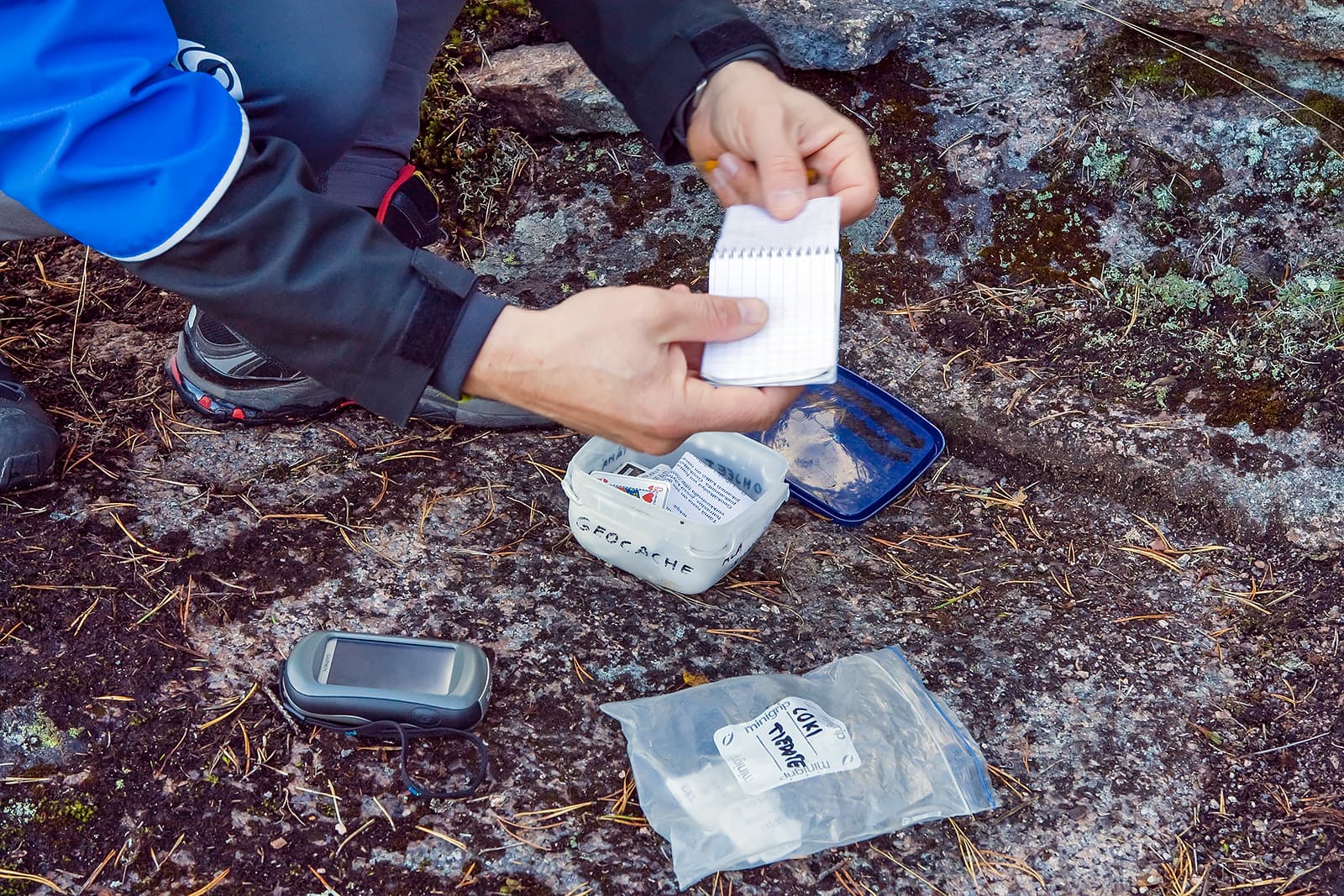 Bild: Jari Kostet Mannen har öppnat geocachen och undersöker innehållet.