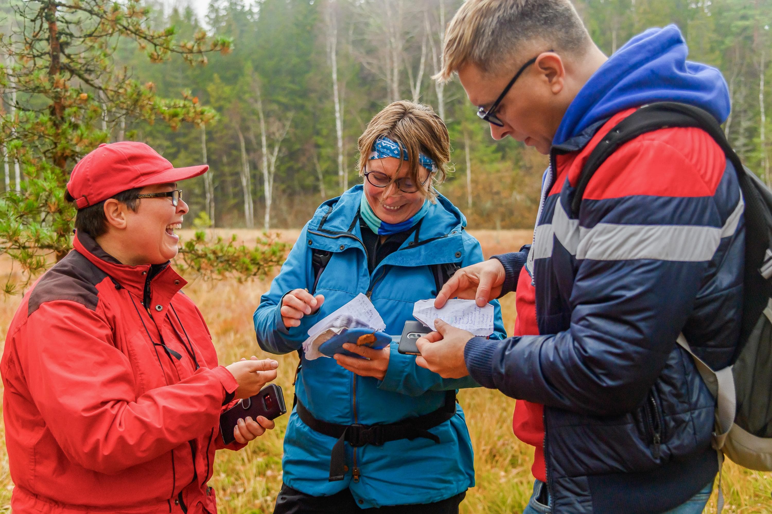 Bild: Jasmin Järvelä Tre vandrare står ansikte mot ansikte och undersöker en geocache de hittat vid kanten av en myr.