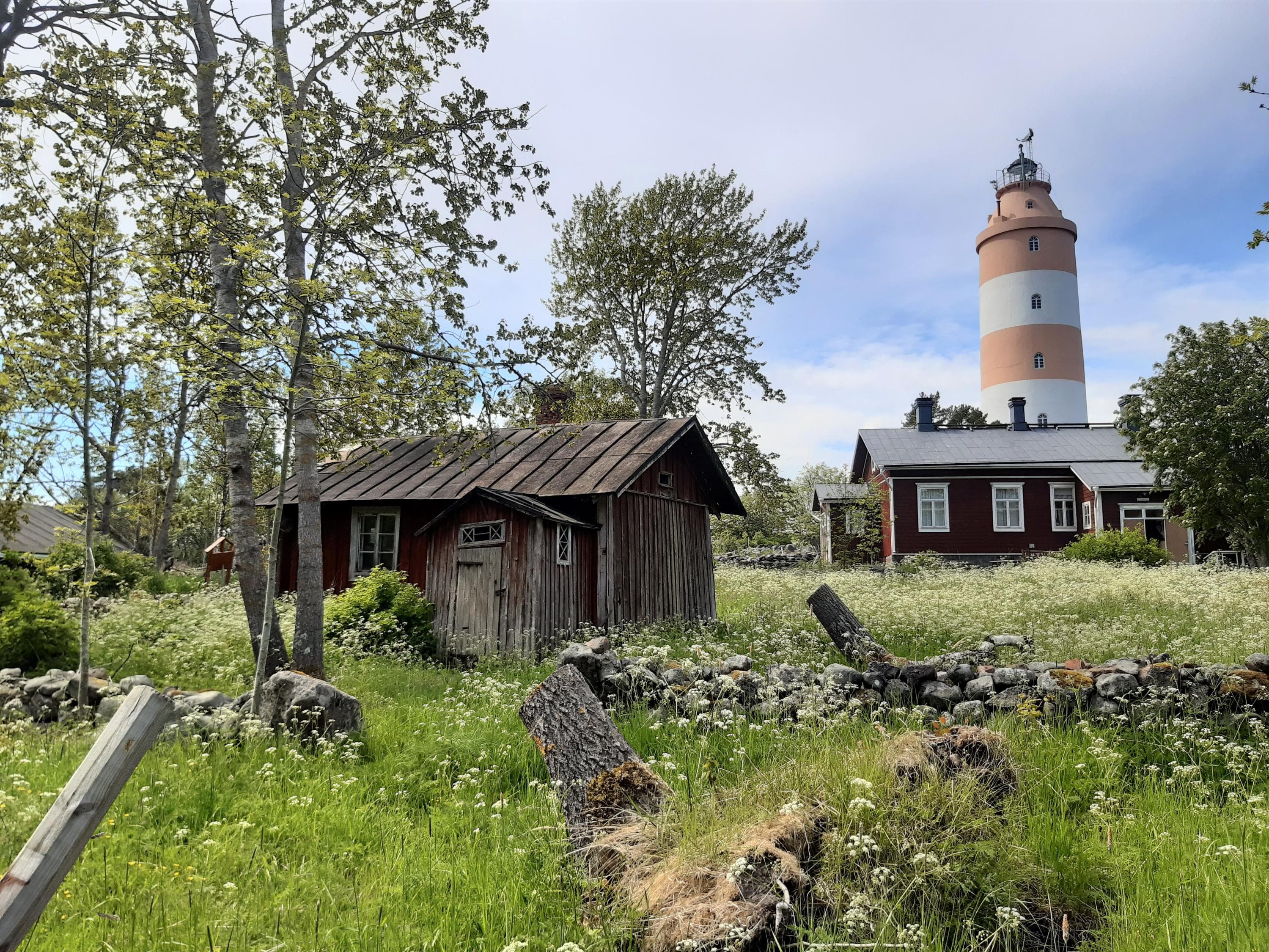 Image: Kirsi Nikkola Red-painted wooden buildings, with a red and white striped lighthouse in the background.