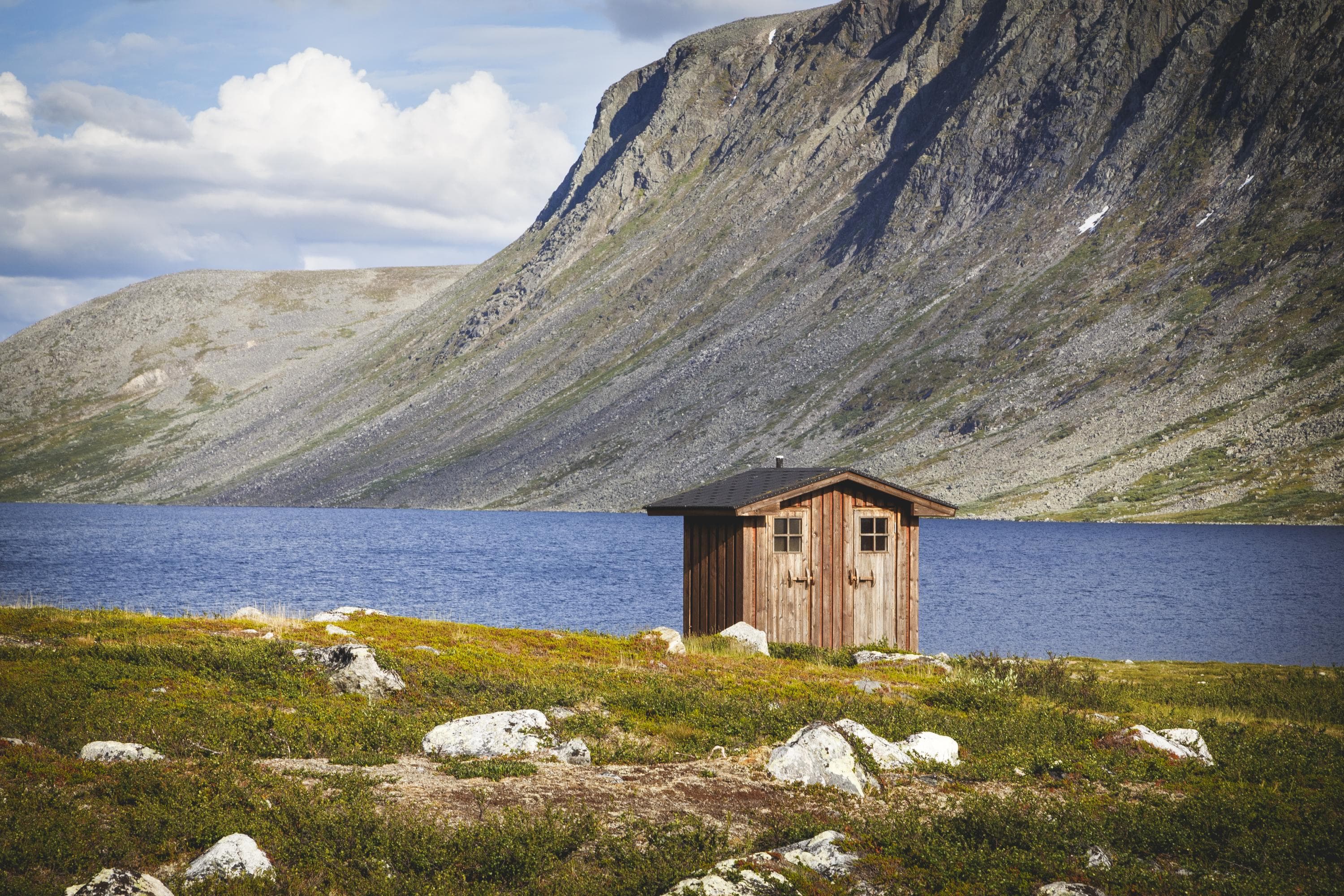 Image: Veli-Pekka Heikkilä / Vastavalo Pieni kaksi ovinen rakennus rannalla kesällä. Vastarannalla kohoaa tunturi.