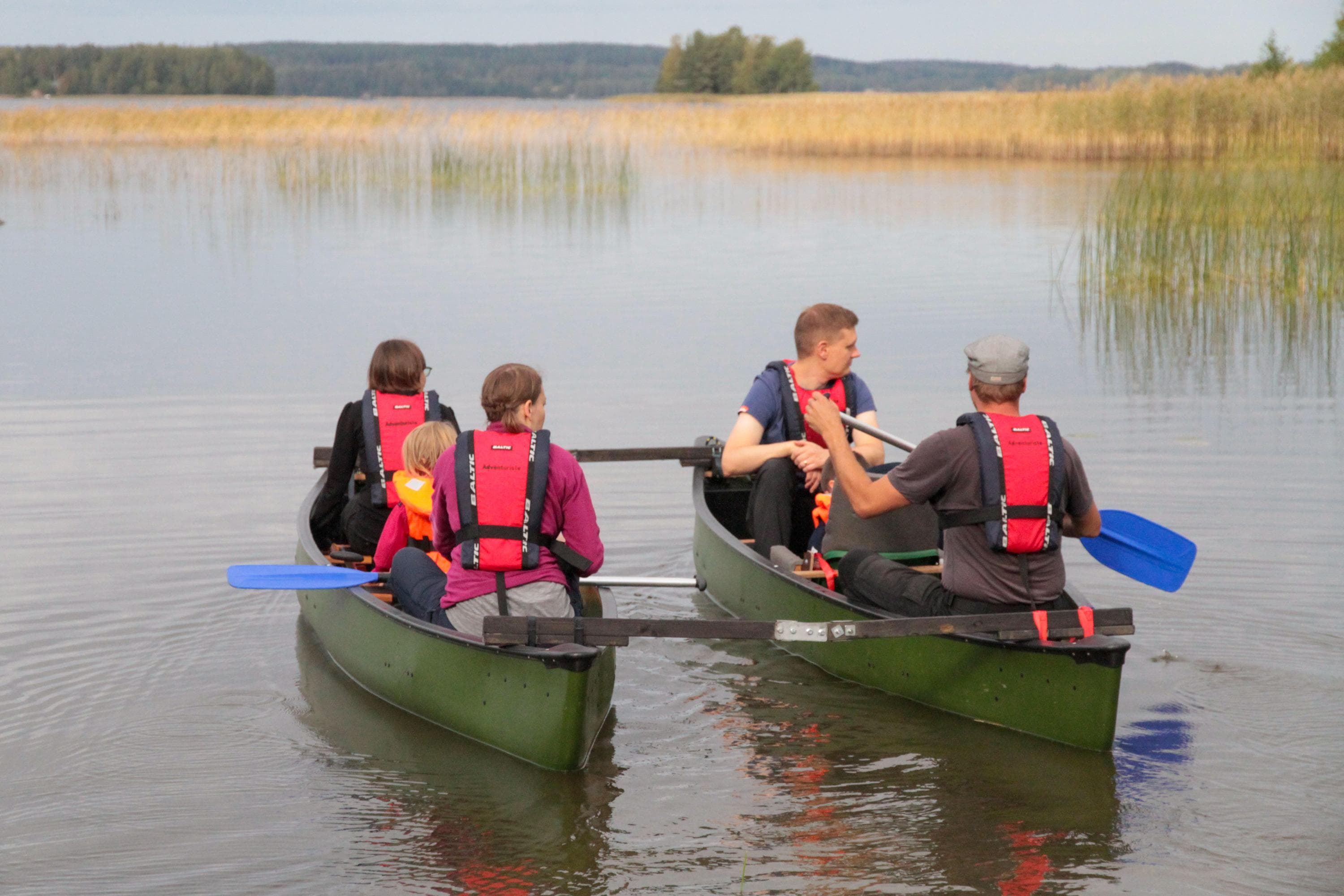 Kuva: Anemone Aaltonen Neljä henkilöä kahdessa vihreässä kanootissa vedessä. Jokaisella on punainen pelastusliivi ja mela. Taustalla näkyy kaislikkoa ja puita.