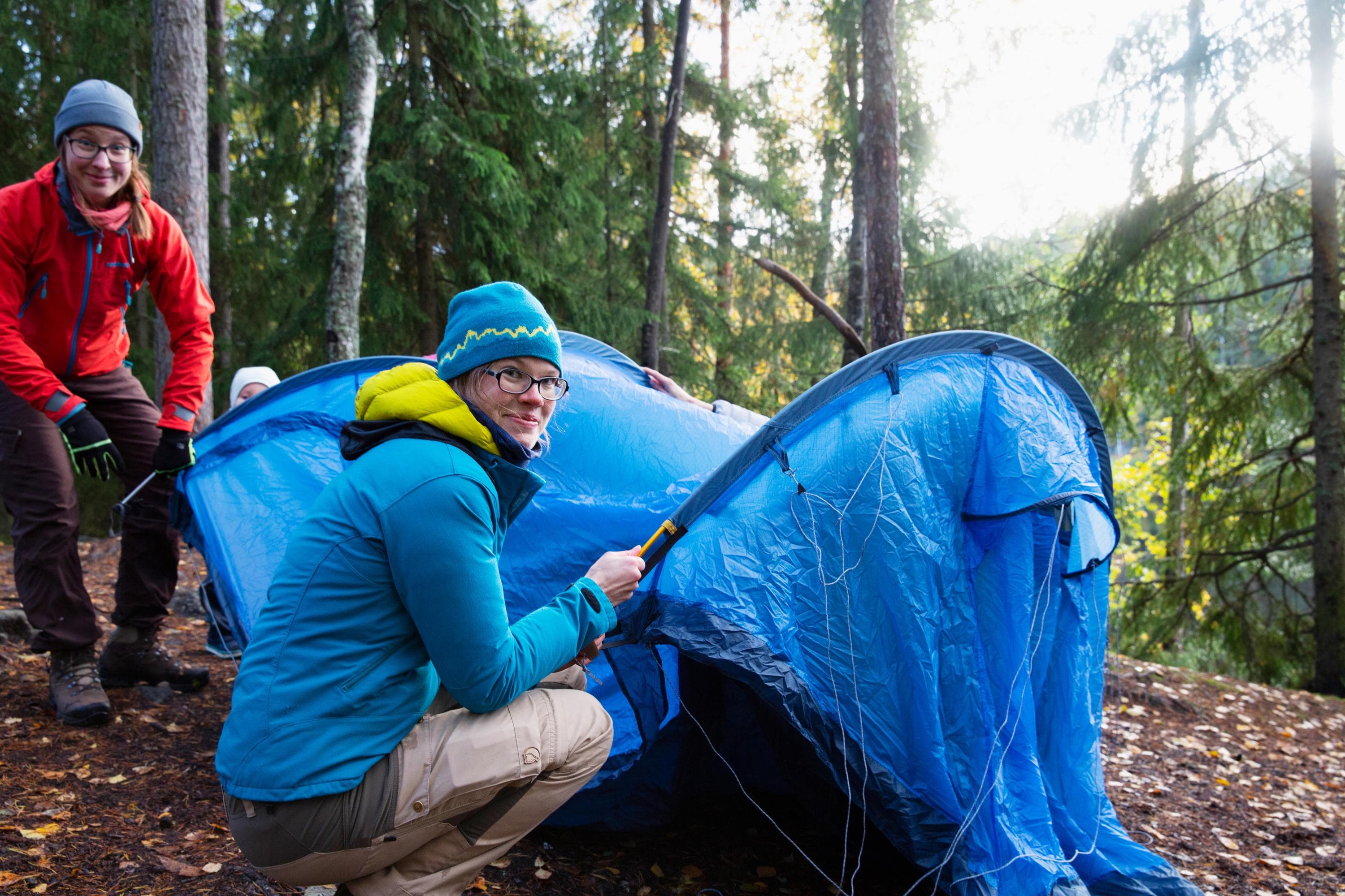 Kuva: Katri Lehtola / Metsähallitus Hymyilevät retkeilijät pystyttämässä telttaa syksyisessä metsässä.