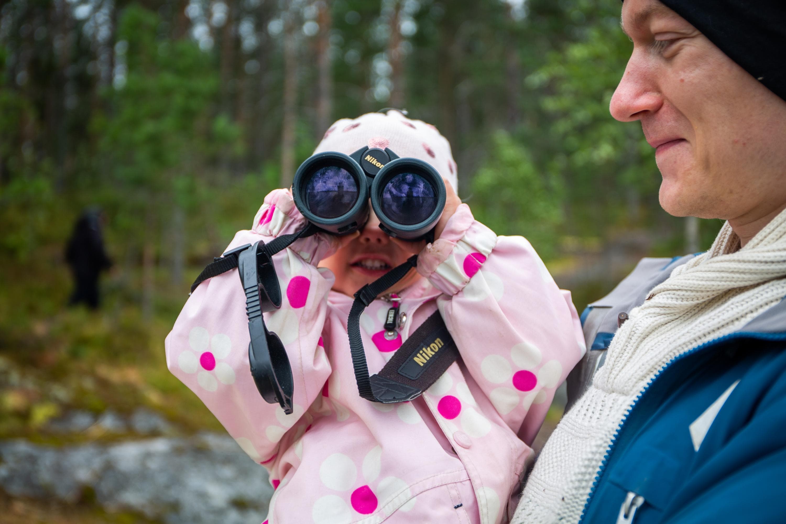 Kuva: Saara Lavi Lapsi katsoo kiikareilla. Aikuinen seisoo vieressä. Taustalla metsää.