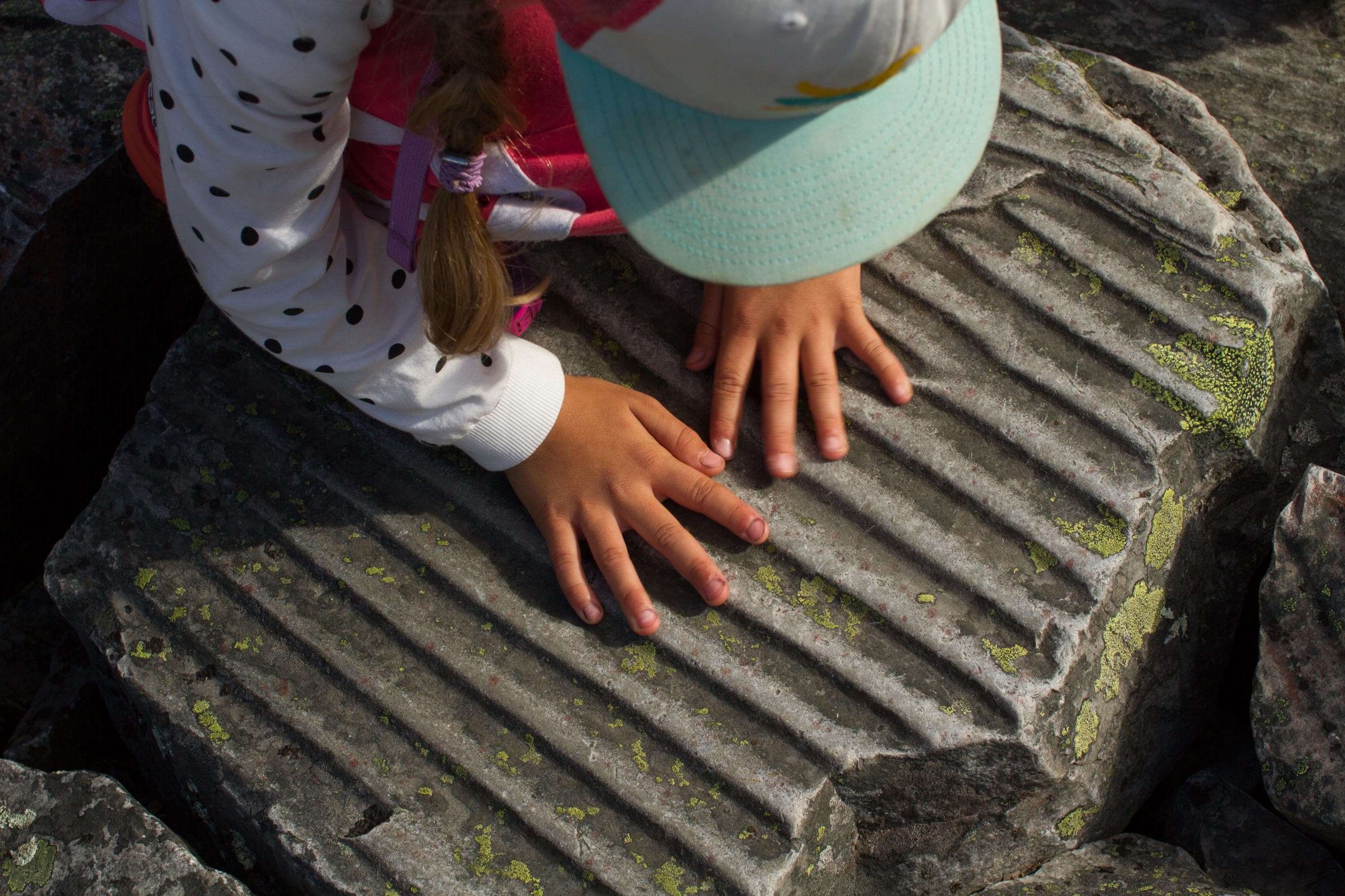 Kuva: Erkki Ollila Ylhäältä kuvattuna lapsi tunnustelee sormilla uurteista kiveä.