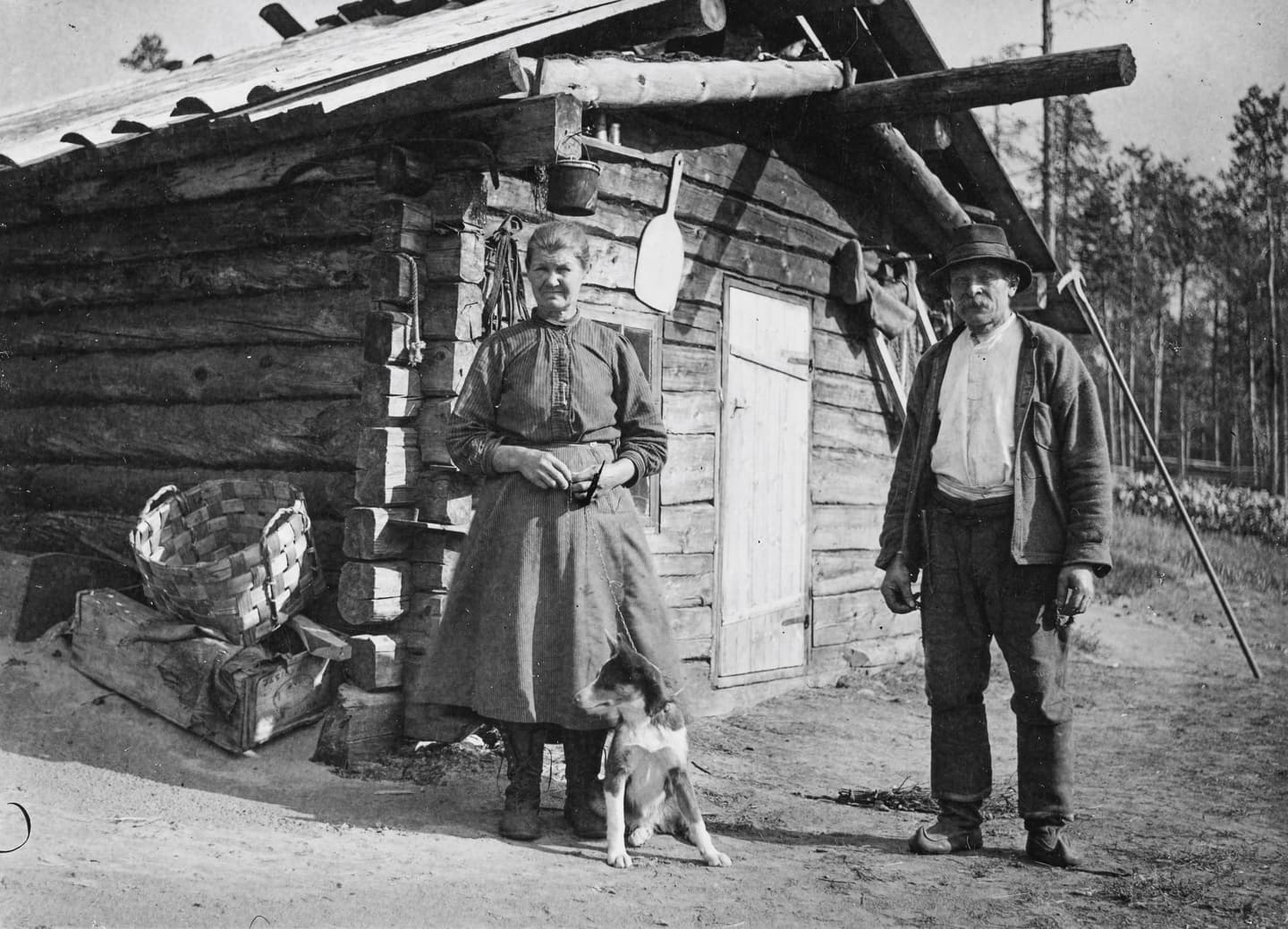 Kuva: Erkki Mikkola Tuvan edustalla seisoo nainen ja mies. Nainen pitää kiinni kettingillä koiraa, joka istuu naisen edessä.