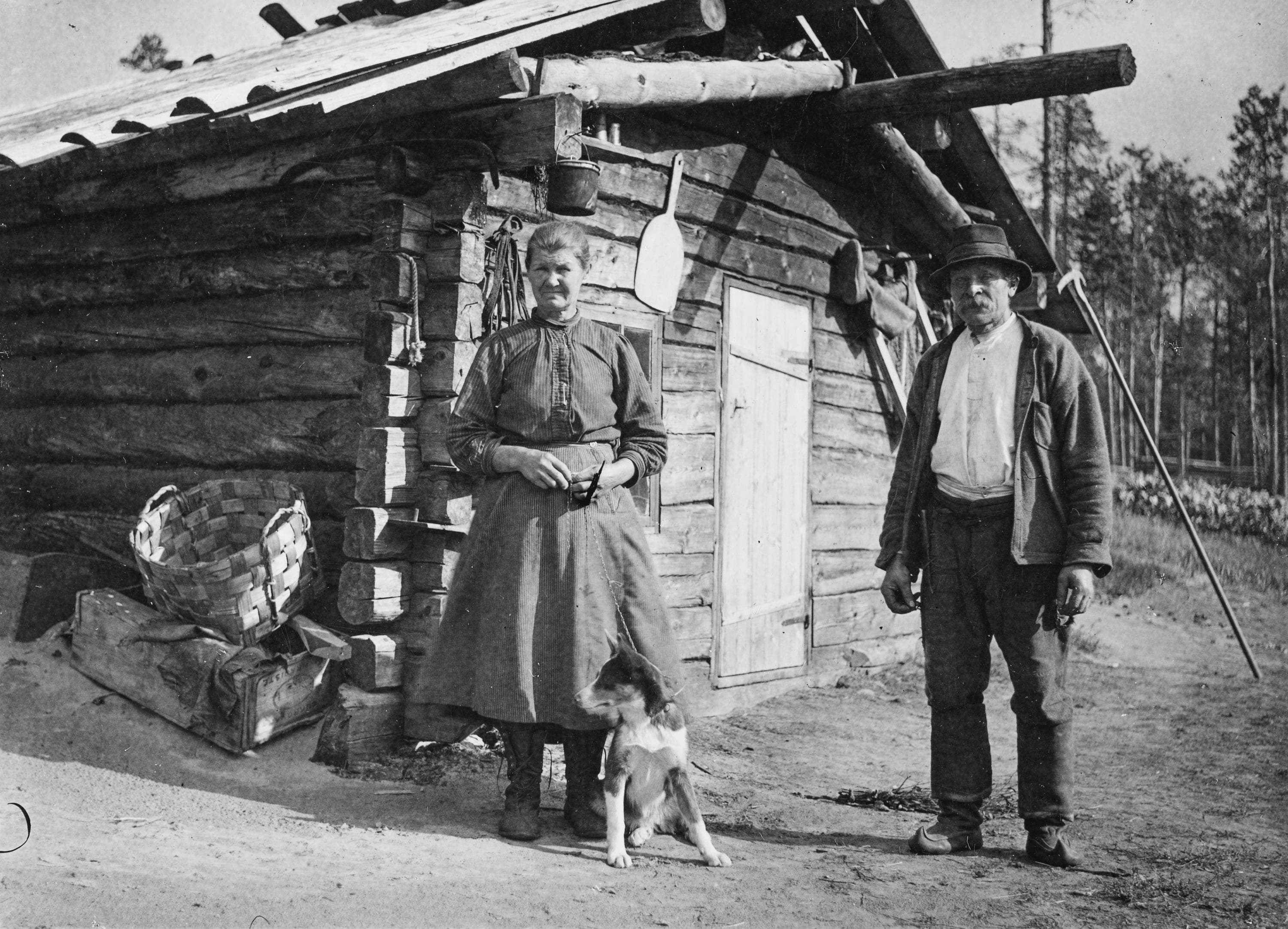 Kuva: Erkki Mikkola Tuvan edustalla seisoo nainen ja mies. Nainen pitää kiinni kettingillä koiraa, joka istuu naisen edessä.