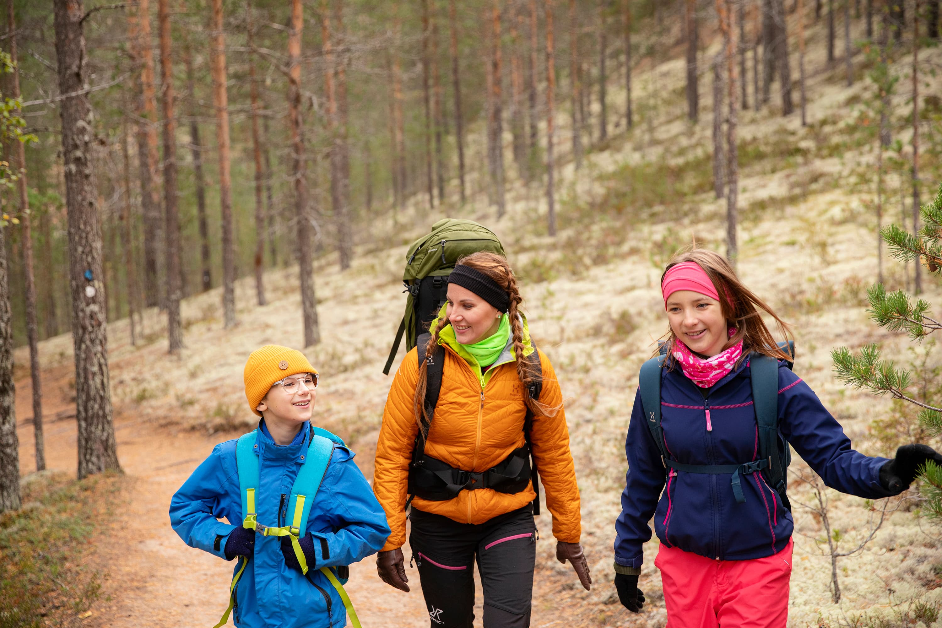 Kuva: Harri Tarvainen Kolme retkeilijää, aikuinen ja kaksi lasta, polulla. Taustalla valkoista jäkäläkangasta ja mäntymetsää.