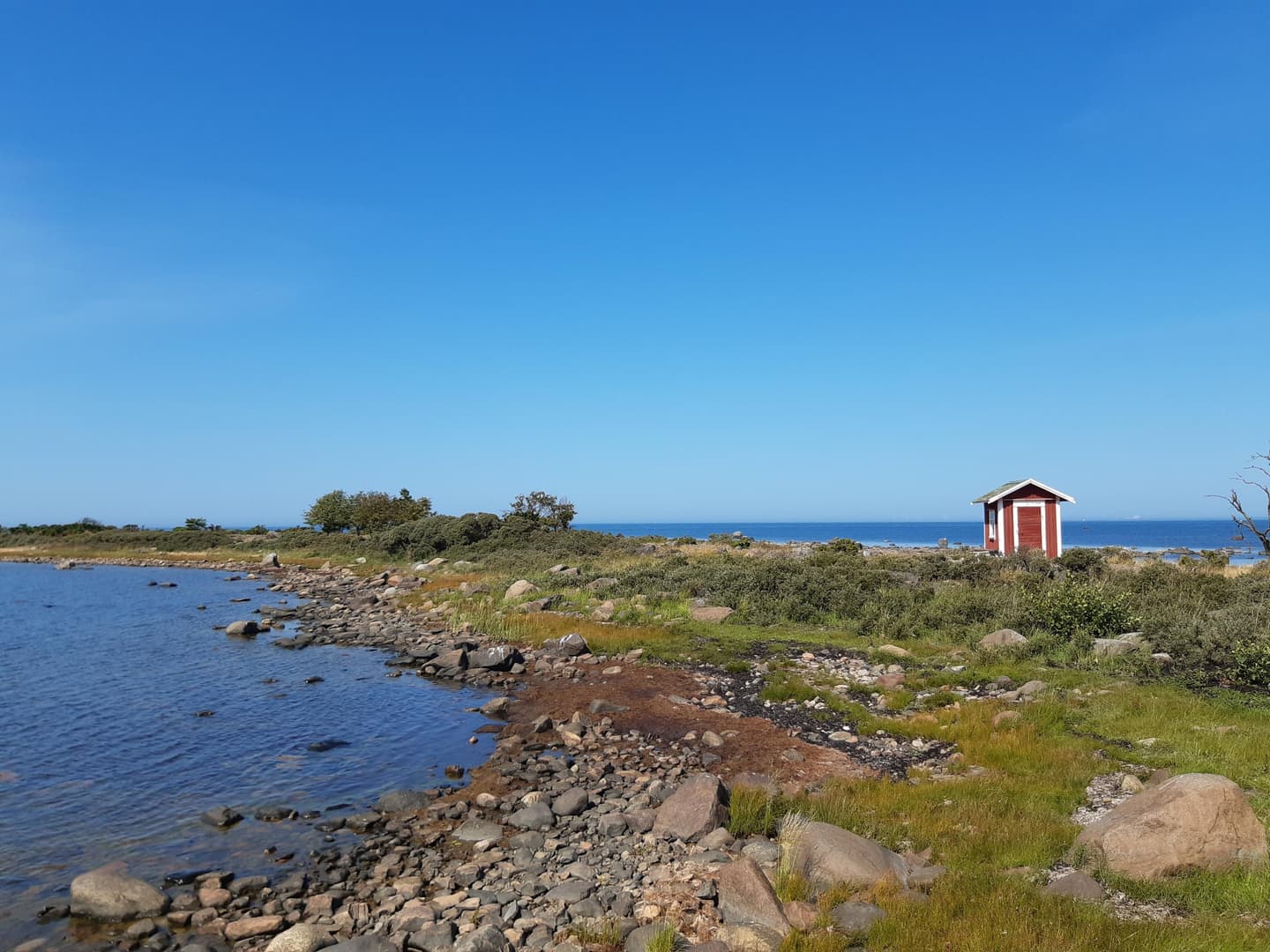 Kuva: Kirsi Nikkola Karu matala merenranta saaressa, kaukana näkyy pieni punainen talo.