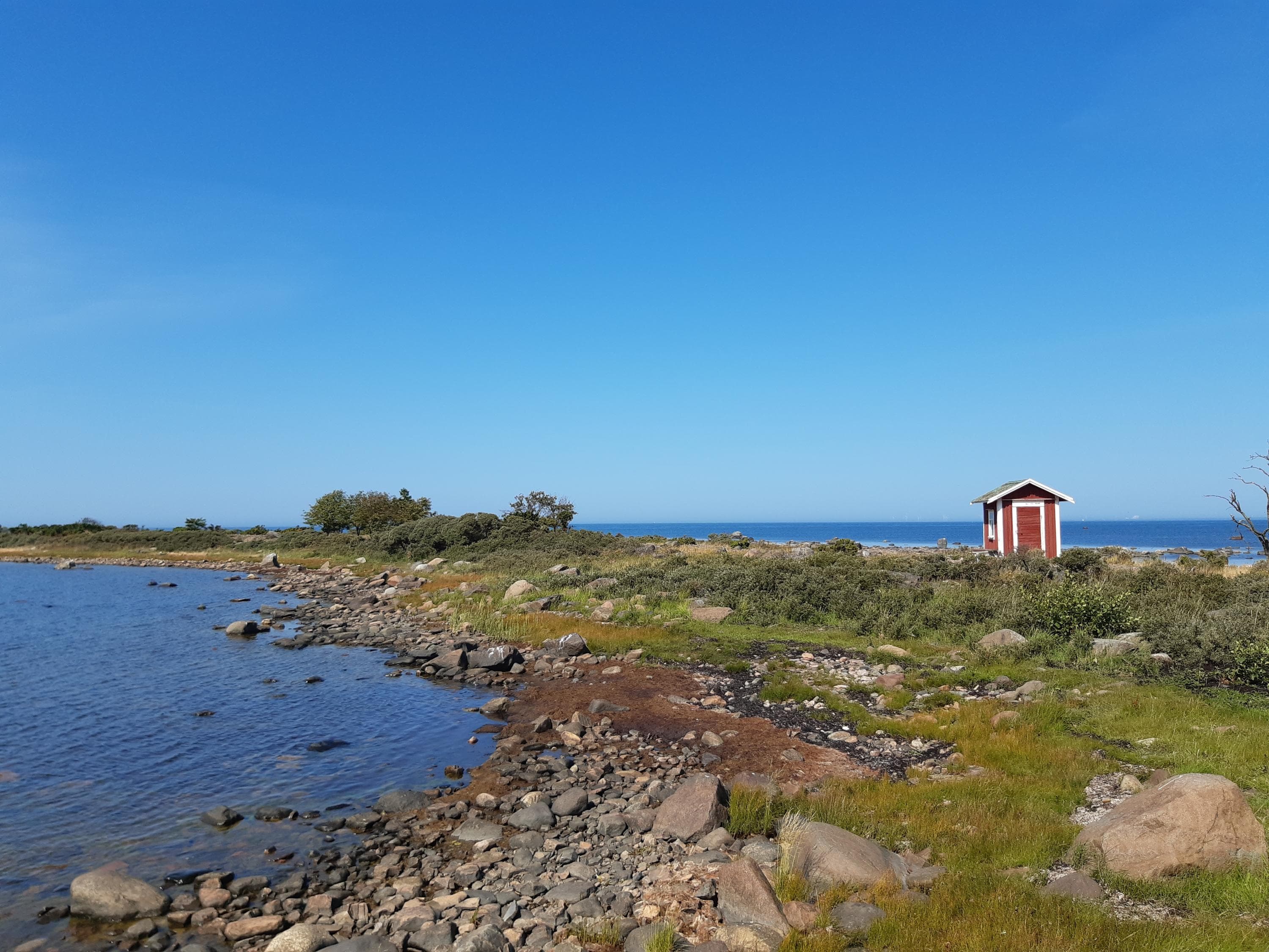 Image: Kirsi Nikkola A barren low seashore on an island, with a small red house visible in the distance.