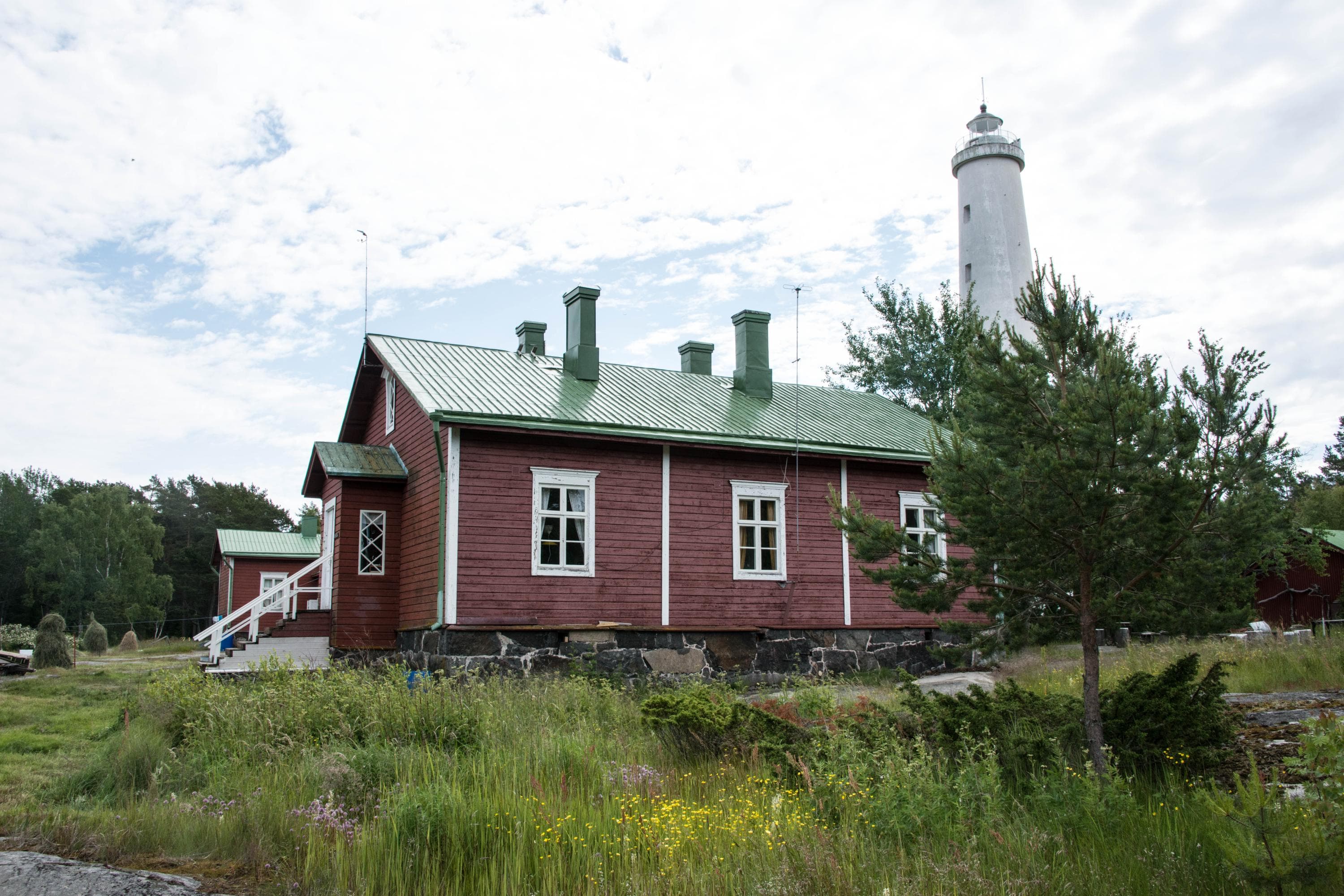 Image: Anssi Riihiaho An old red-painted wooden building, with a white lighthouse behind it.
