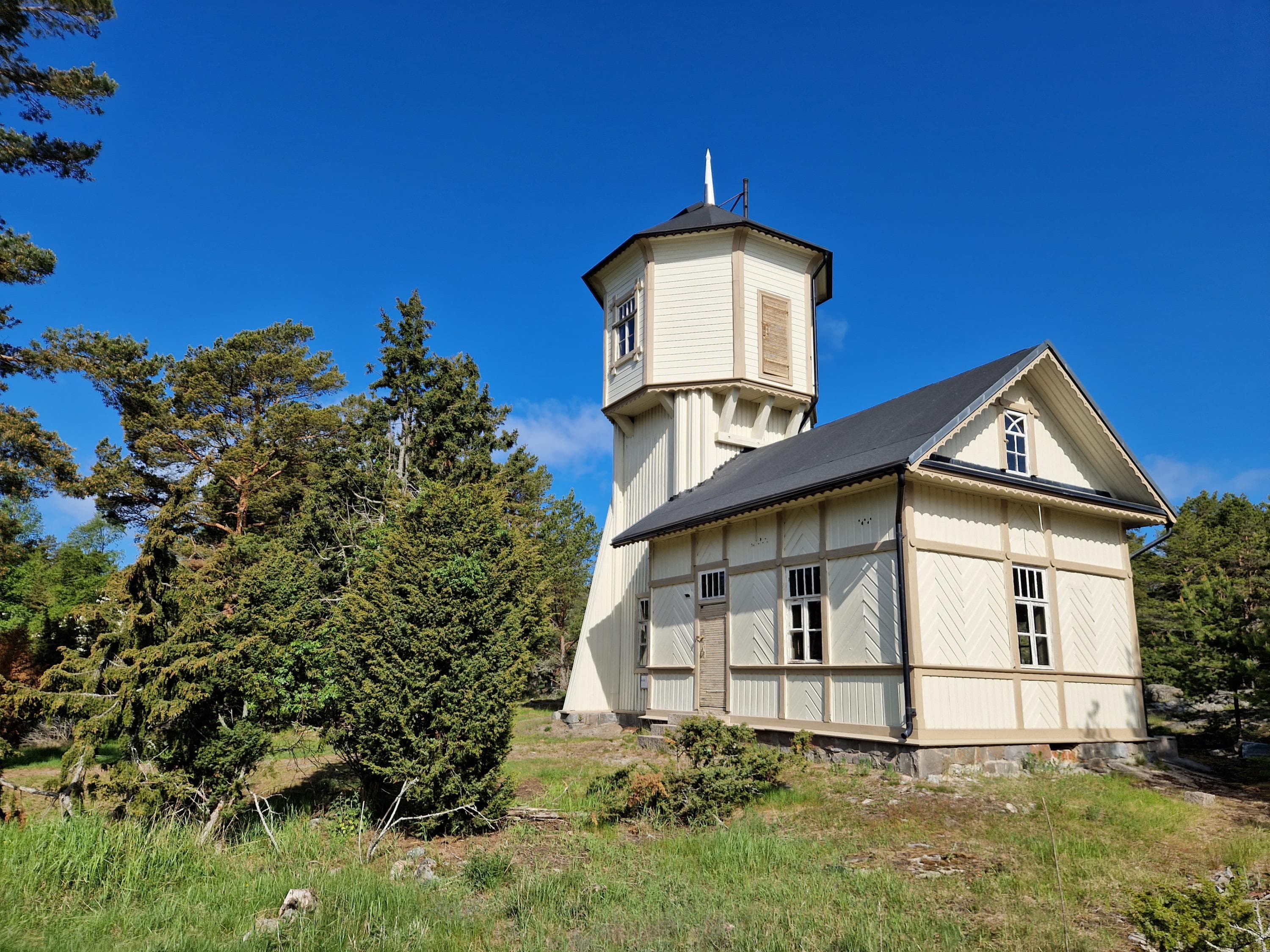 Image: Marjo Kekki A white-painted wooden building with a tall tower. Trees grow around it.