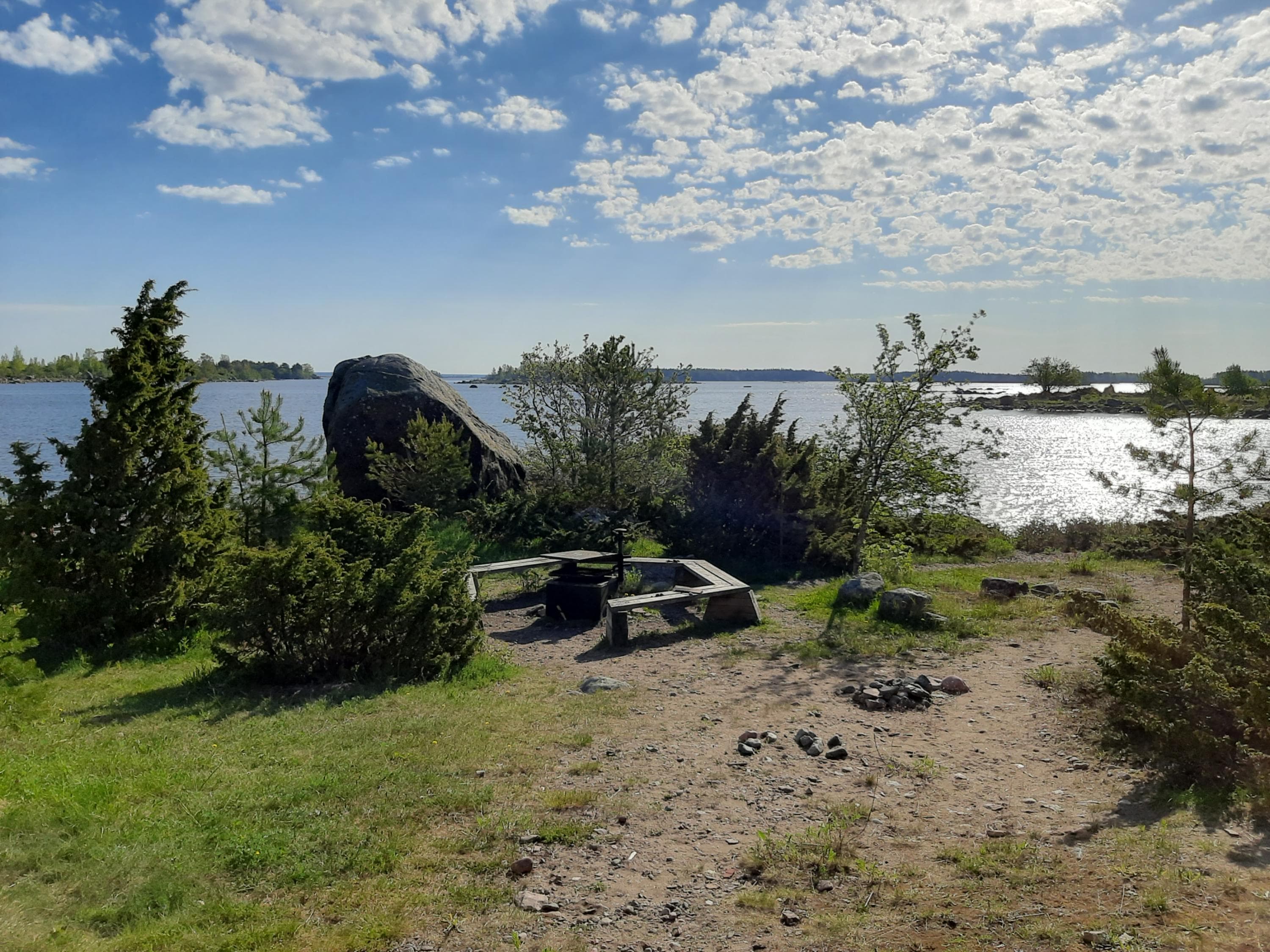 Image: Marjo Kekki Nuotiopaikka jonka ympärillä on penkit. Maasto on kallioista, ympärillä kasva muutamia matalia pensaita, taustalla näkyy meri.
