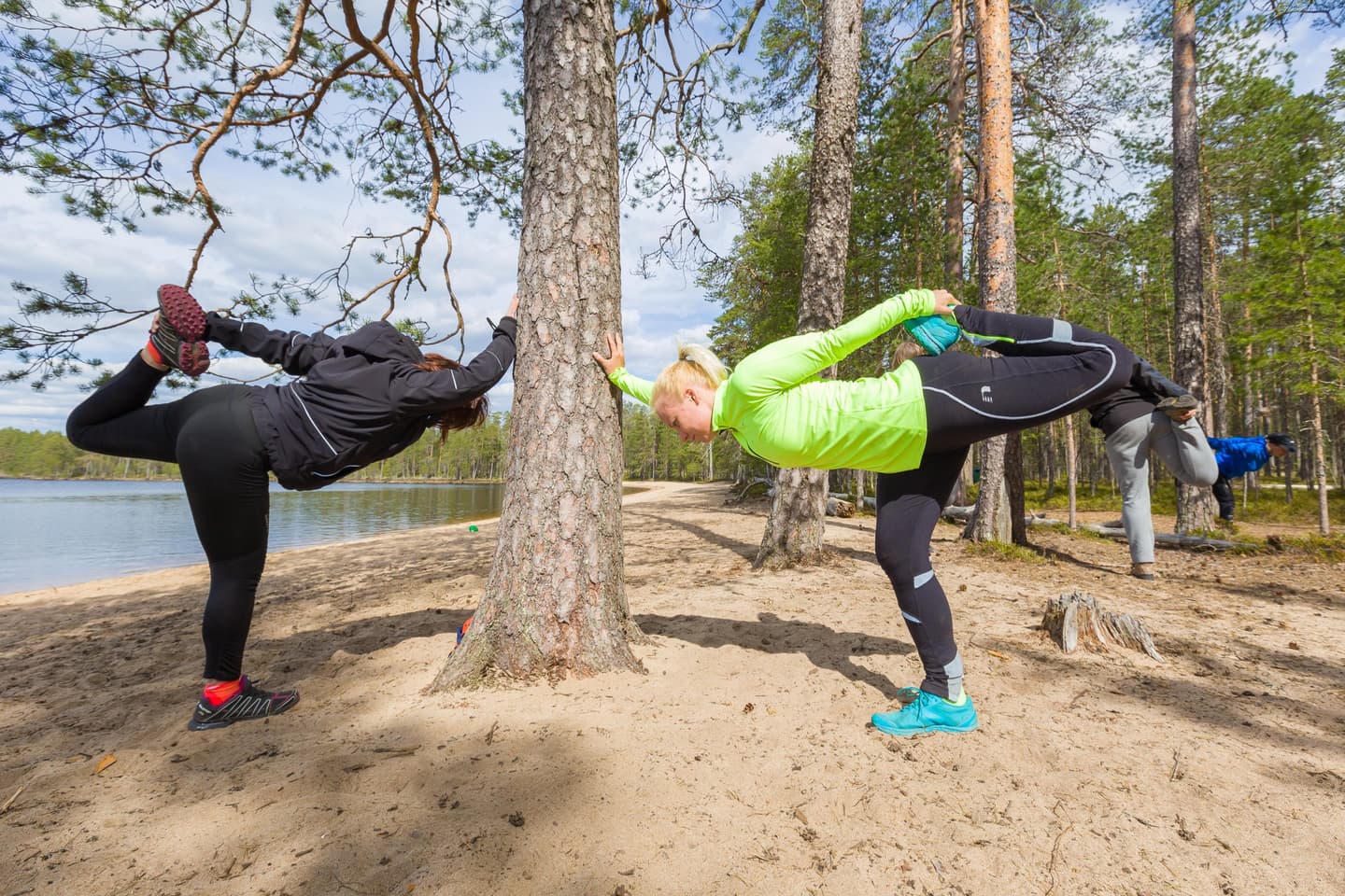 Bild: Petri Jauhiainen Vandrare som stretchar på en sandstrand. I bakgrunden en somrig sjöutsikt och skog.