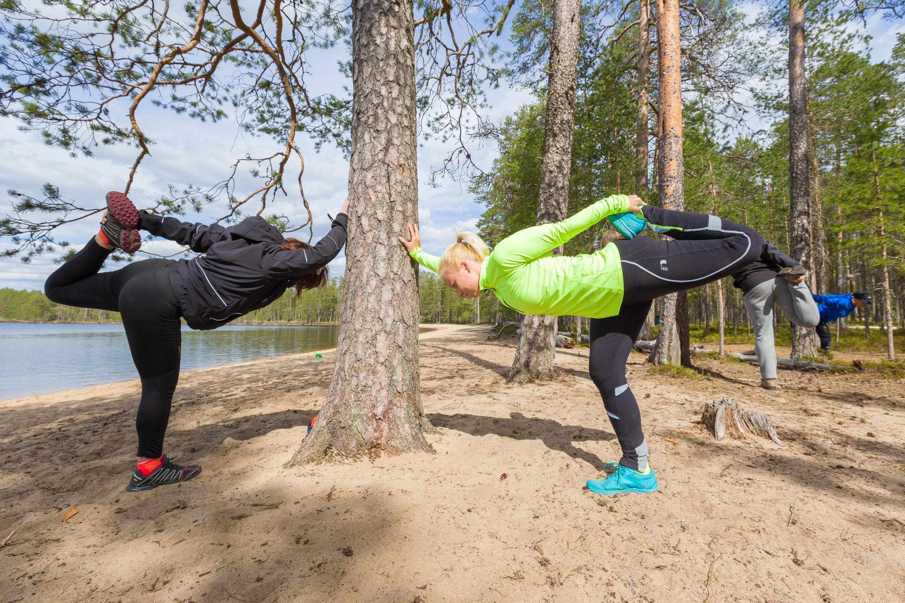 Kuva: Petri Jauhiainen Retkeilijöitä venyttelemässä hiekkarannalla. Taustalla kesäinen järvimaisema ja metsää.