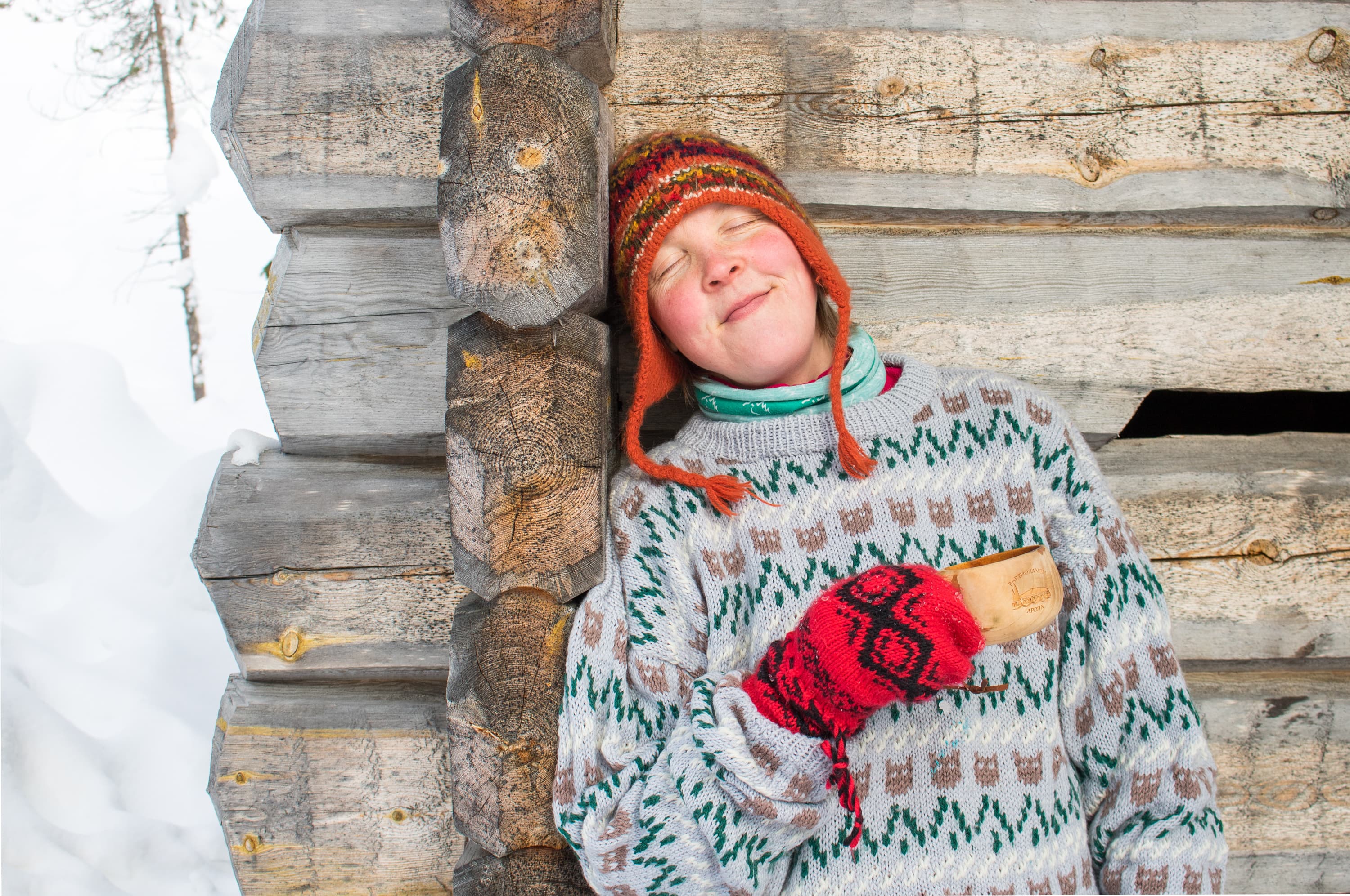 Kuva: Sini Salmirinne Hymyilevä retkeilijä nojaa hirsirakennuksen seinään.