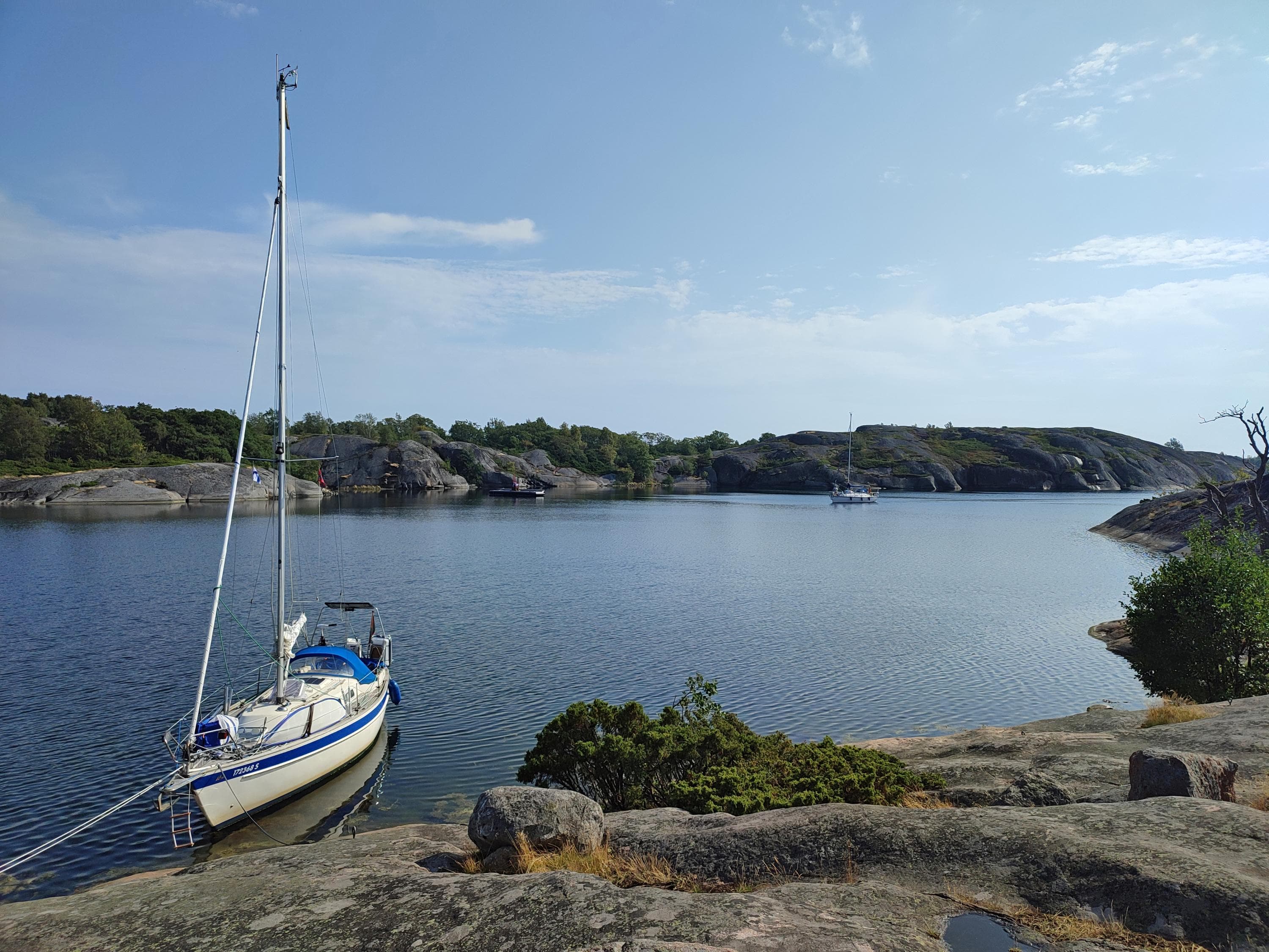 Image: Jussi Helimäki Sailboat moored to a cliff. In the calm bay sailboat in motion, with cliffs in the background.